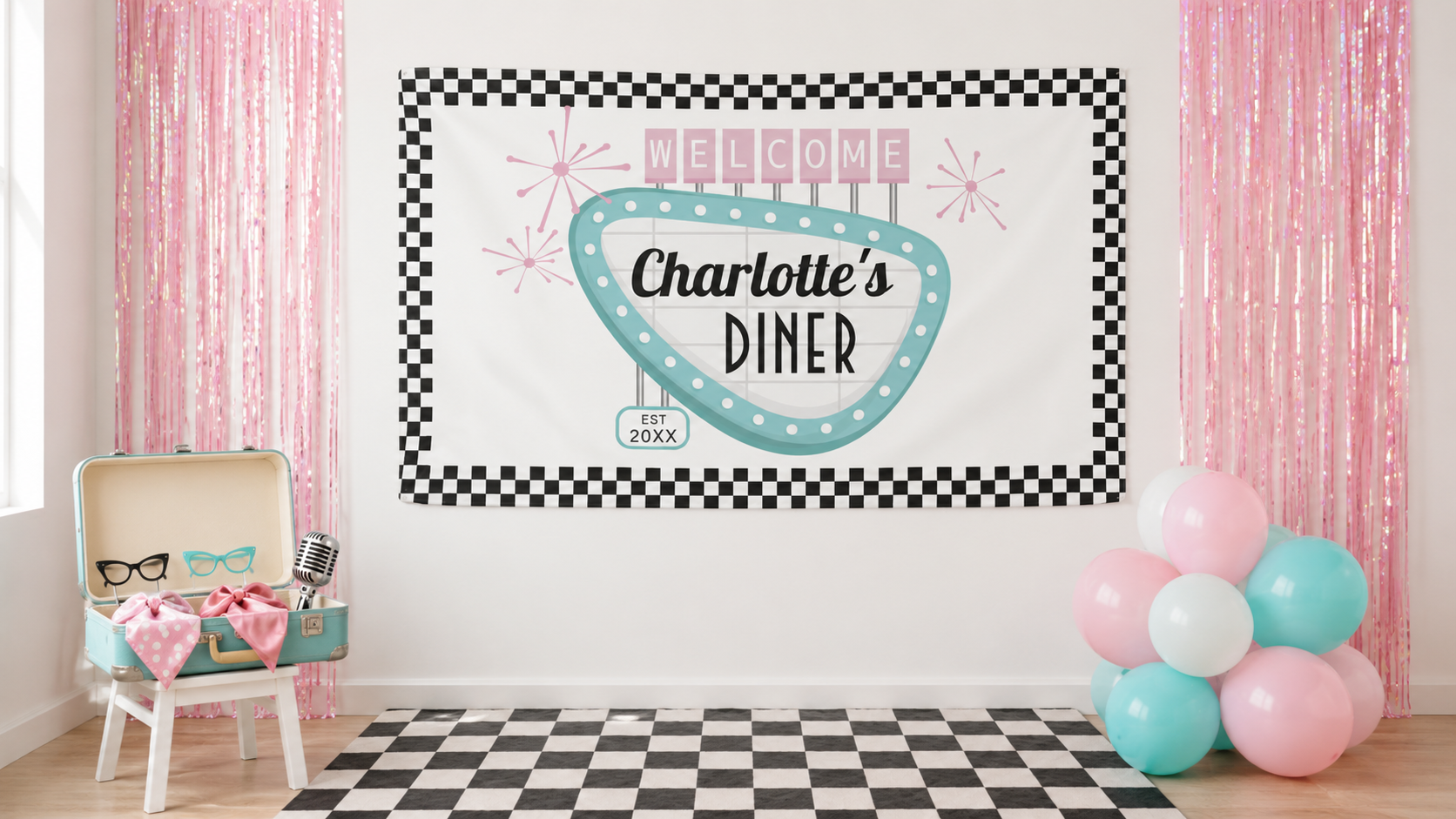 Sock hop photo booth with a personalized Charlotte’s Diner banner, pink fringe, retro props, pastel balloons, and a checkerboard rug.