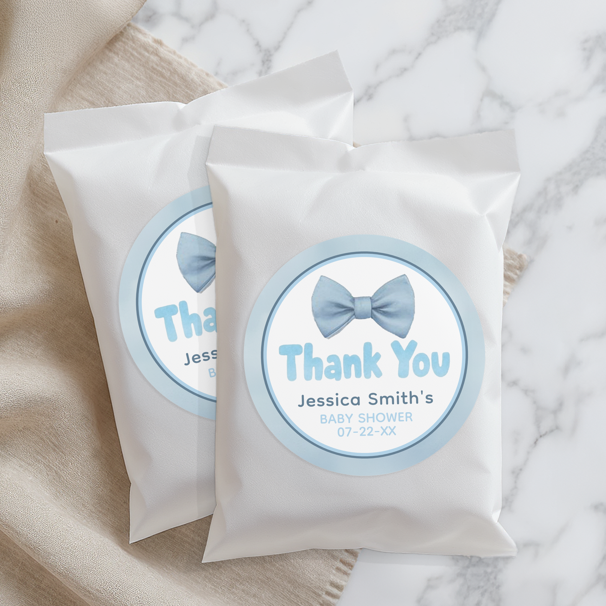 Personalized blue bow tie baby shower thank you stickers on white favor treat bags, perfect for guest favors.