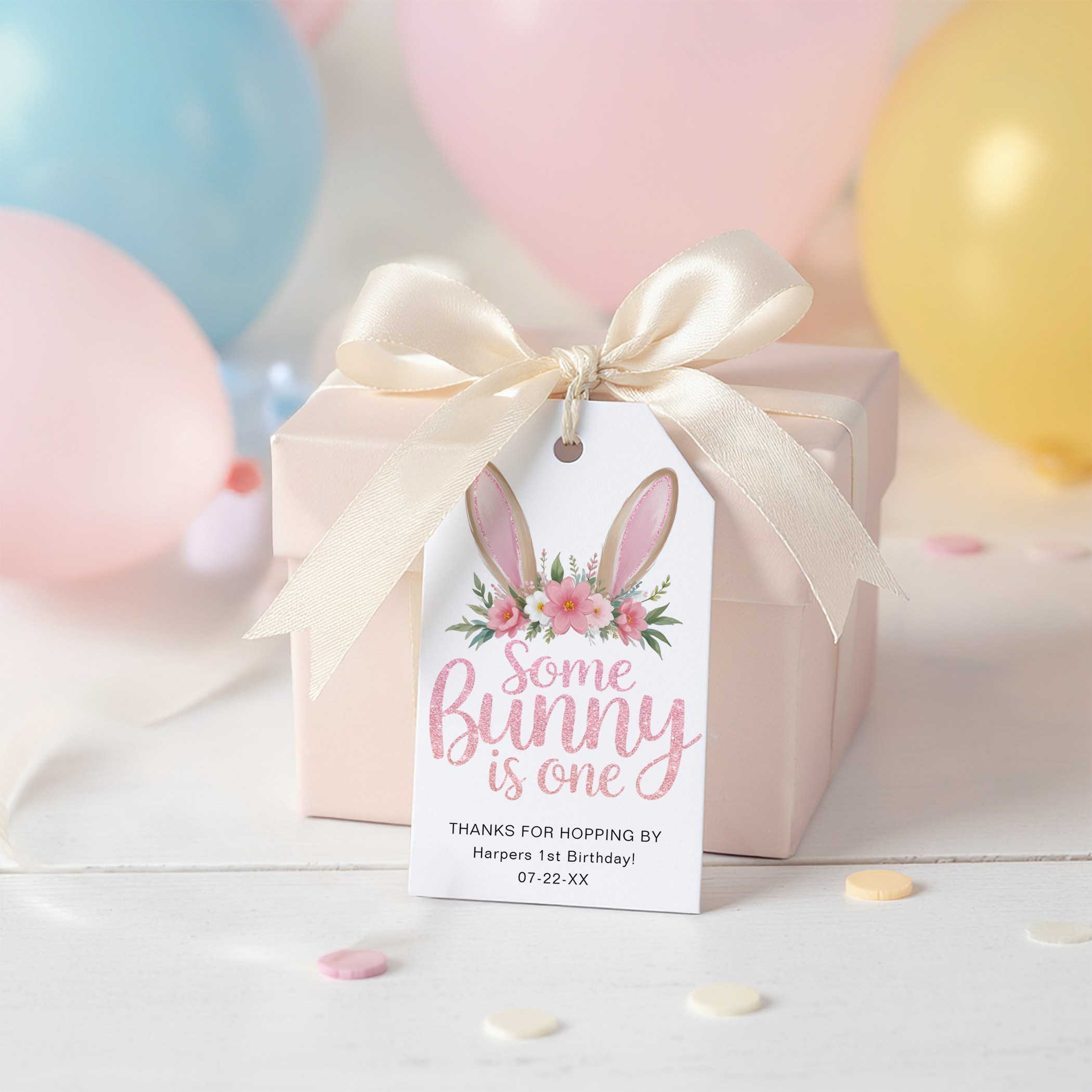 Some Bunny Is One birthday favor tag with bunny ears and pink florals tied onto a pastel gift box with ribbon.