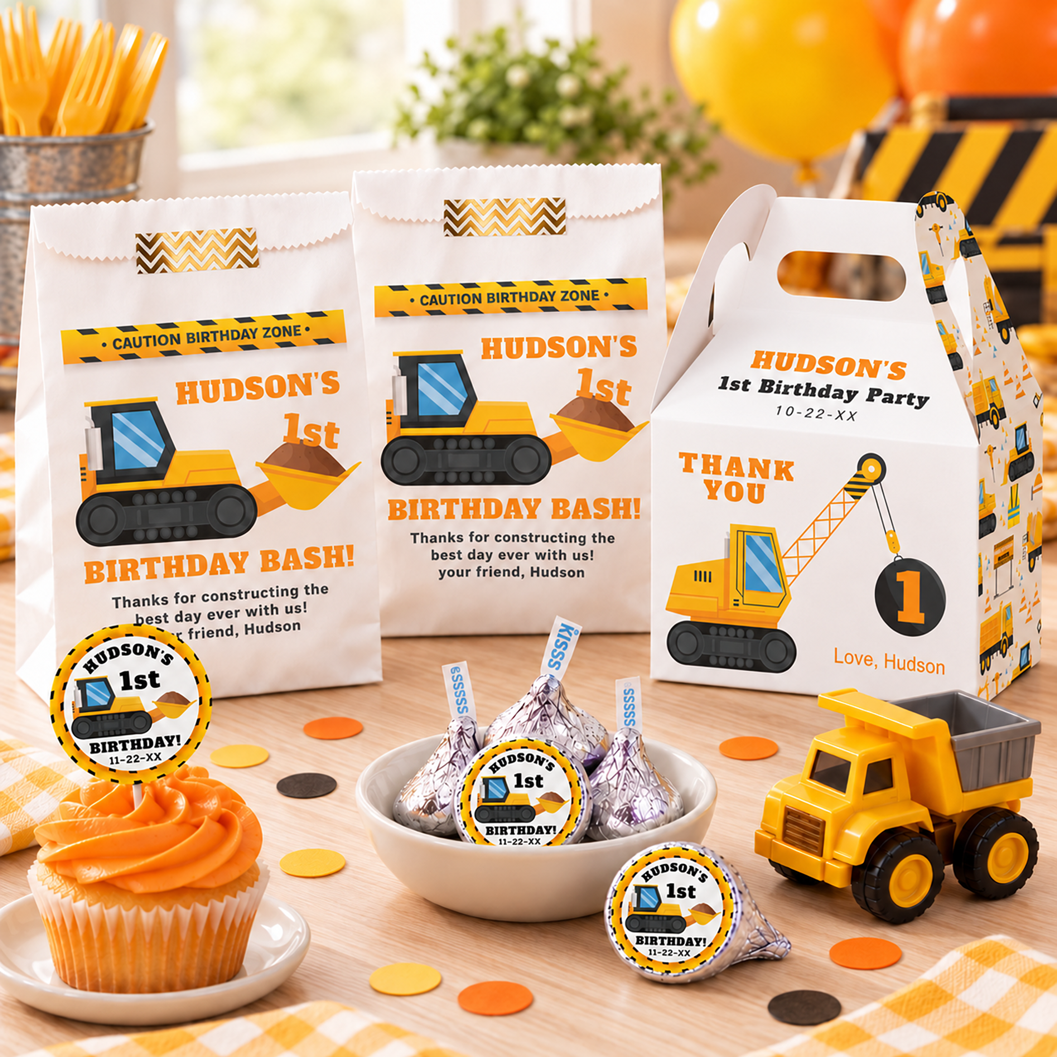 Construction birthday party favors with personalized handled gift box, treat bags, cupcake topper, Hershey’s Kisses stickers, toy dump truck, and yellow orange construction decorations.