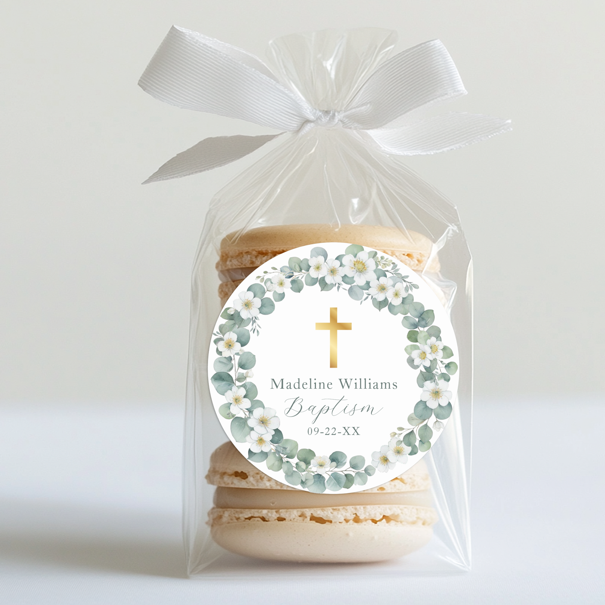 Round baptism favor sticker with gold cross, soft greenery wreath, and personalized name and date.