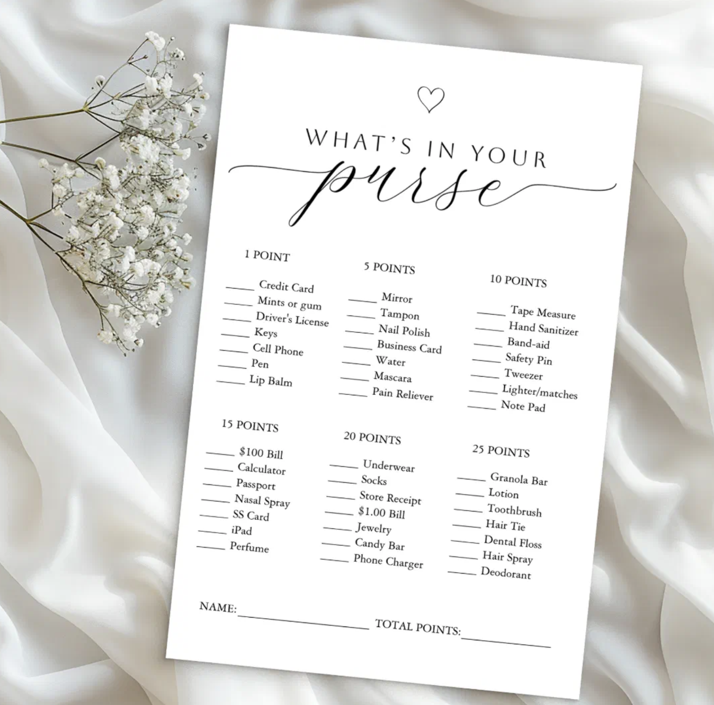 Elegant What’s In Your Purse bridal shower game card displayed on white satin fabric with baby's breath flowers. Minimalist printable bridal shower party game listing purse items with point values in a chic black and white design.