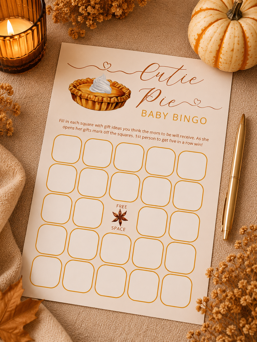 Cutie Pie baby shower bingo game card styled with orange and cream pumpkins, dried florals, autumn leaves, candlelight, and a gold pen for a cozy fall baby shower.