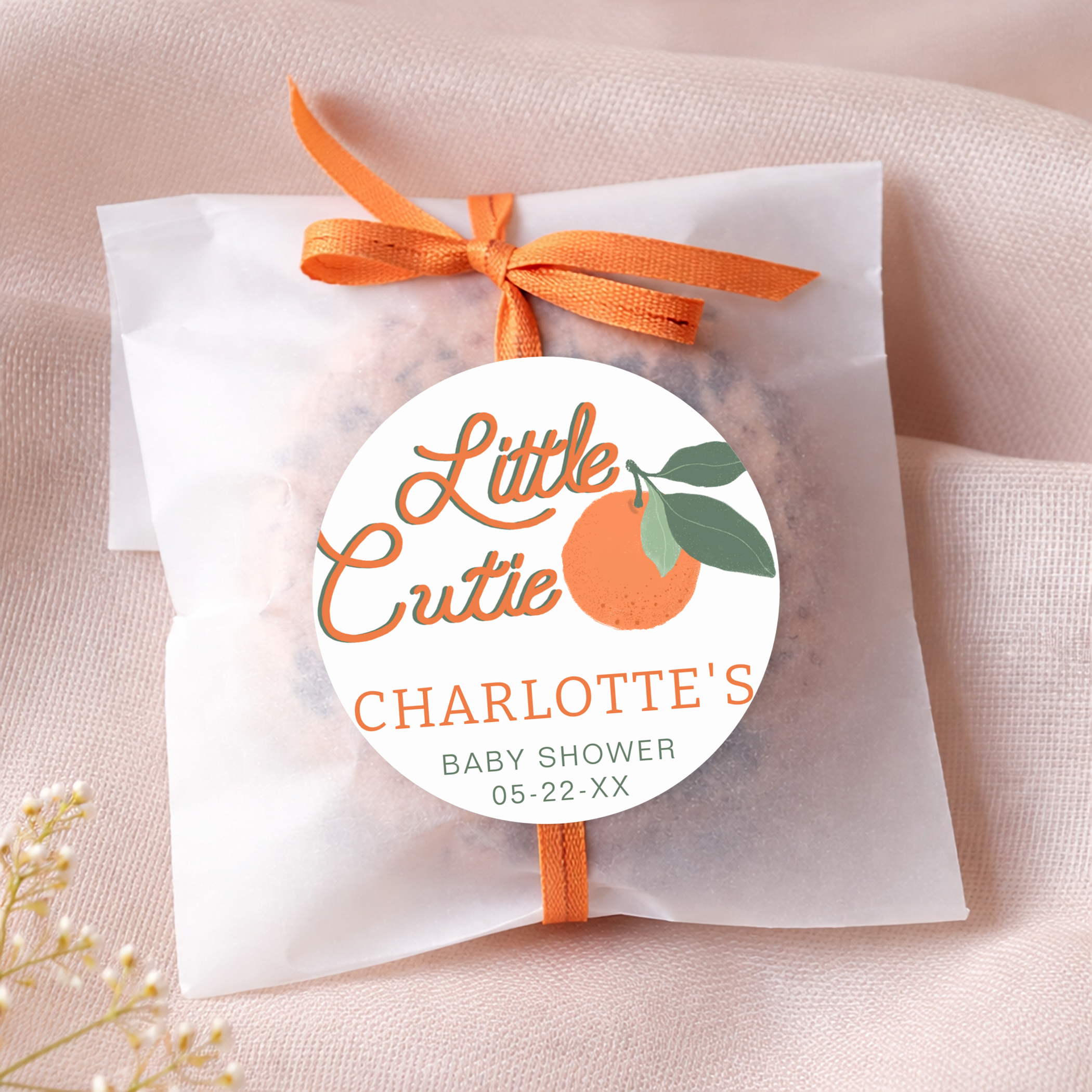 Little Cutie baby shower favor with personalized round citrus sticker on a glassine bag tied with orange ribbon, featuring a clementine theme design