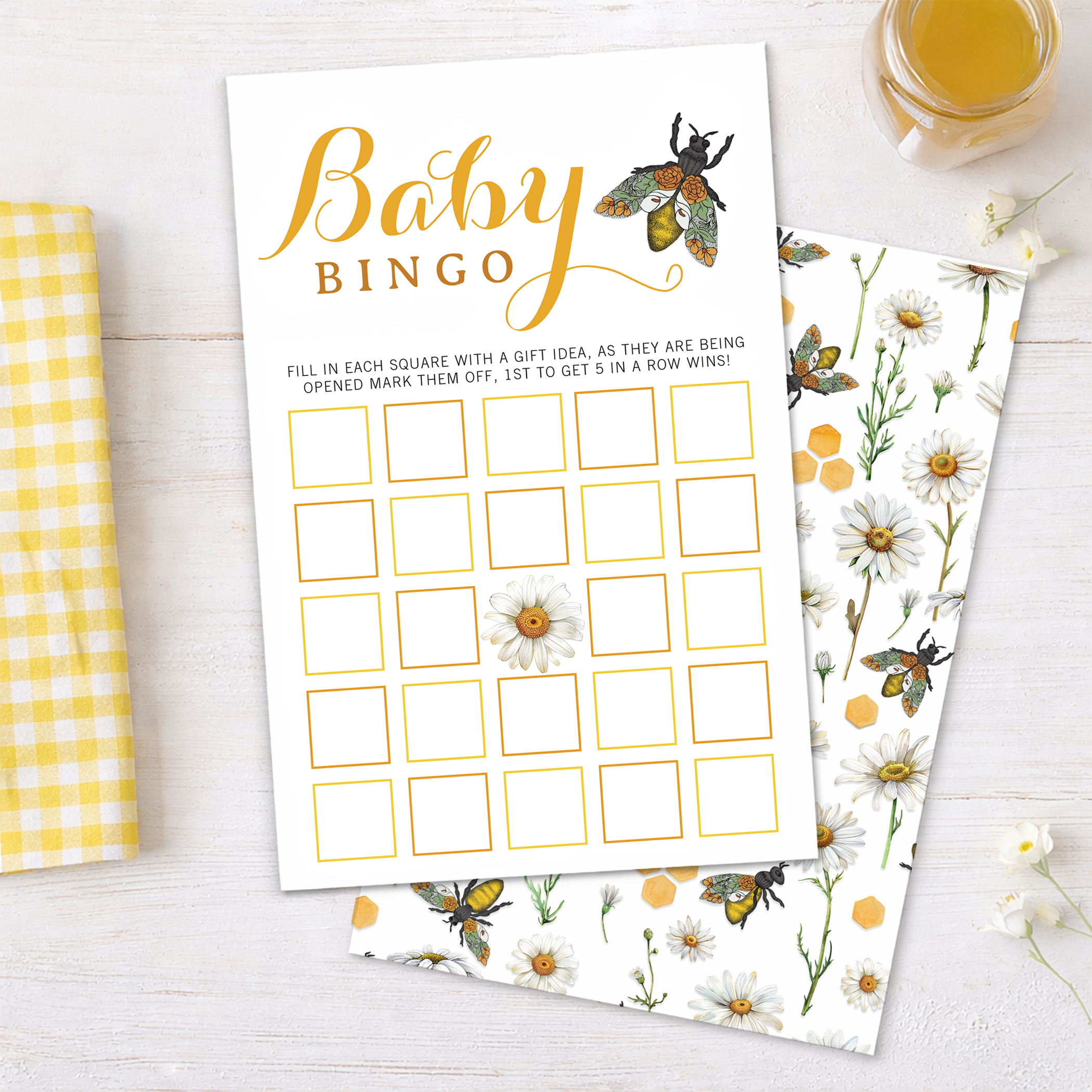 Honey bee themed baby shower bingo game card with watercolor bees, daisies, and honeycomb accents displayed in a flat lay party setting