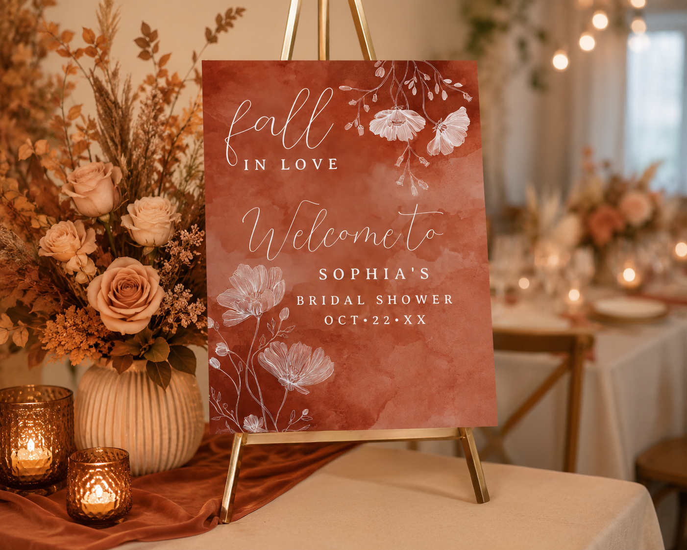 Terracotta fall bridal shower welcome sign with watercolor floral design displayed on a gold easel beside candles and warm autumn flowers.