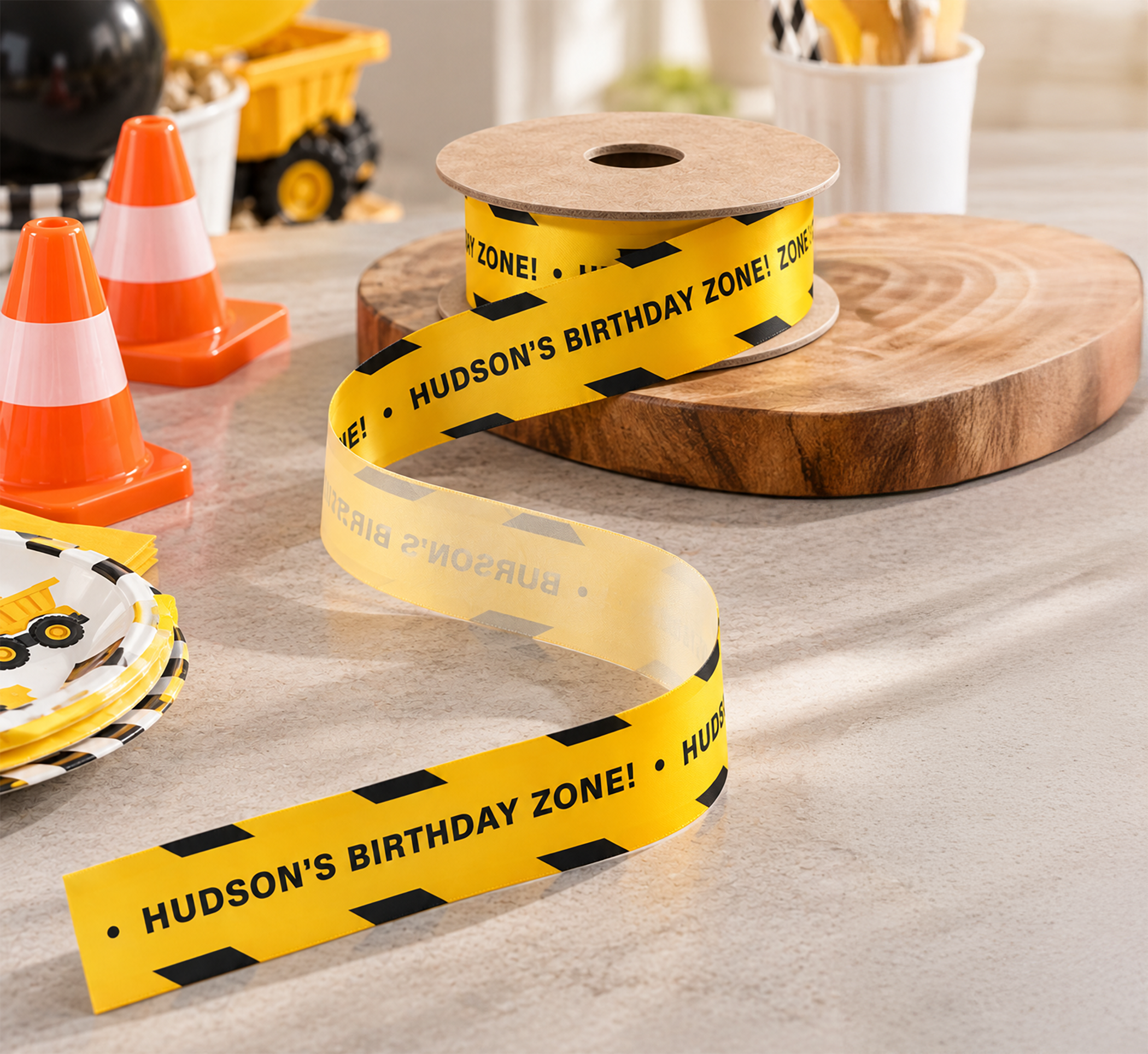Construction birthday decor detail with yellow caution-style ribbon, orange traffic cones, and simple party styling in a yellow, black, and cream color palette.