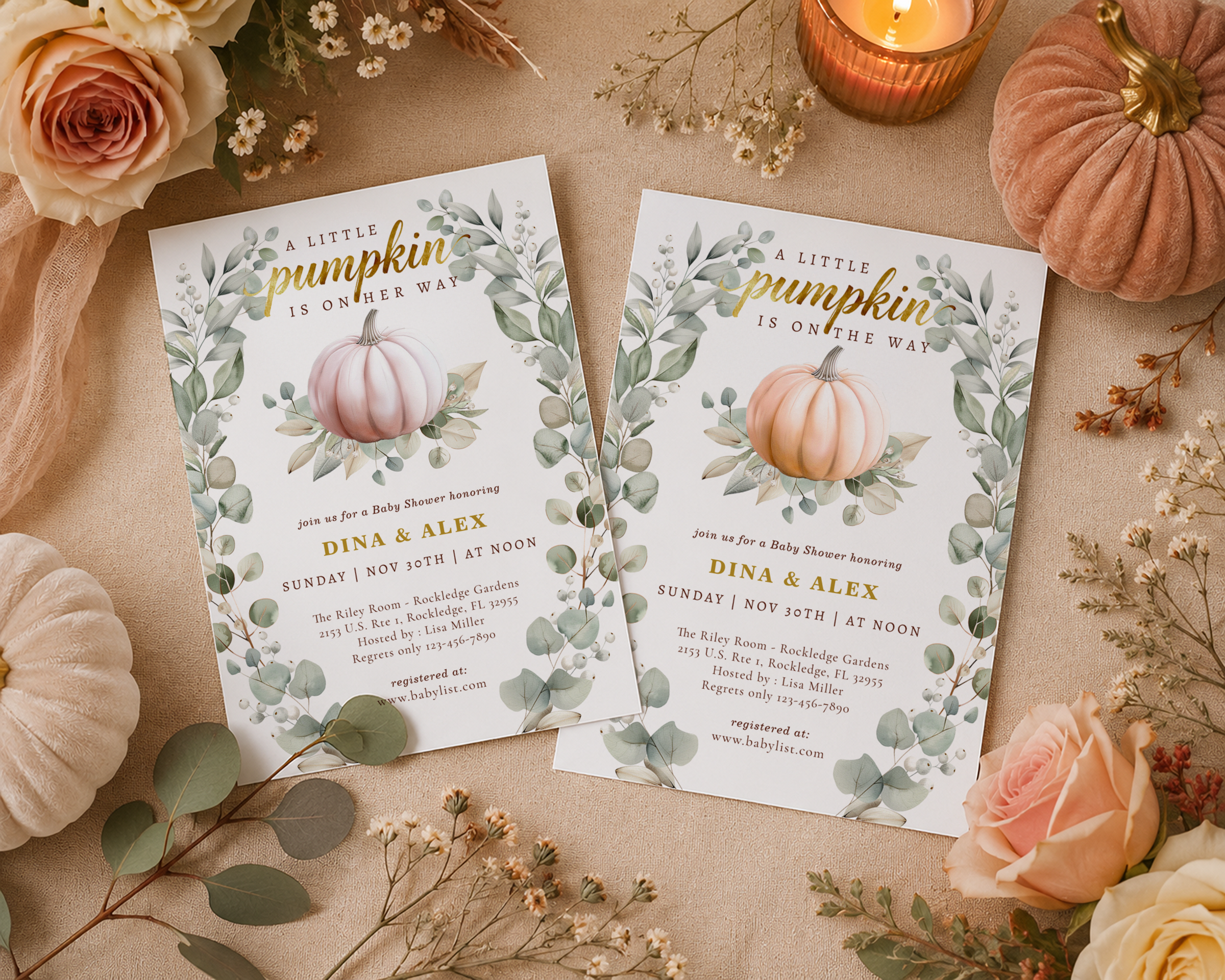 Flat lay of two 5x7 little pumpkin baby shower invitations displayed side by side on a neutral beige fabric surface, featuring blush pink and classic autumn orange pumpkin designs surrounded by candles, roses, eucalyptus, and soft fall décor.
