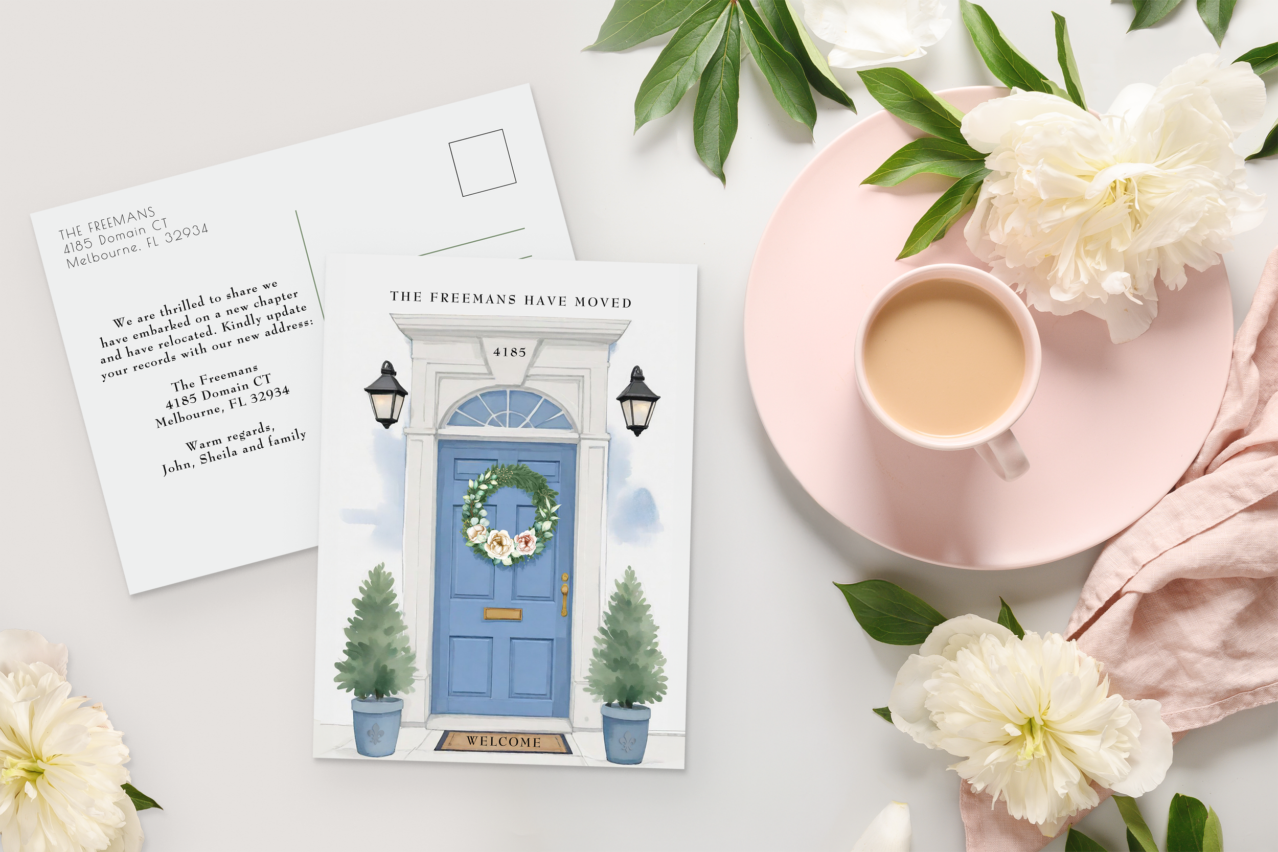 Elegant moving announcement card featuring a watercolor blue front door with a floral wreath, styled with soft flowers and a cup of tea.