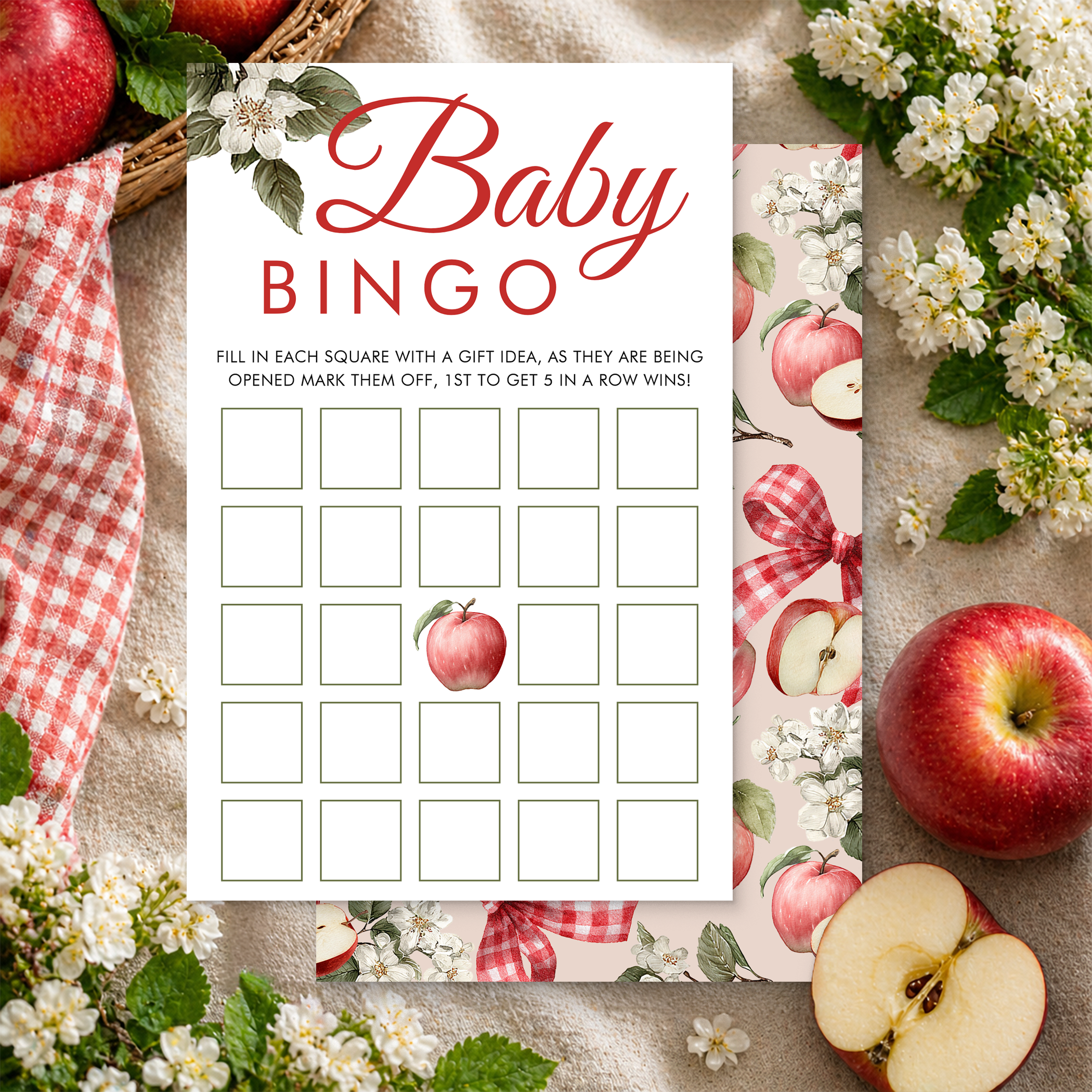Apple blossom-themed Baby Bingo game card styled with fresh apples, white blossoms, and a red gingham ribbon in an editorial flat lay.