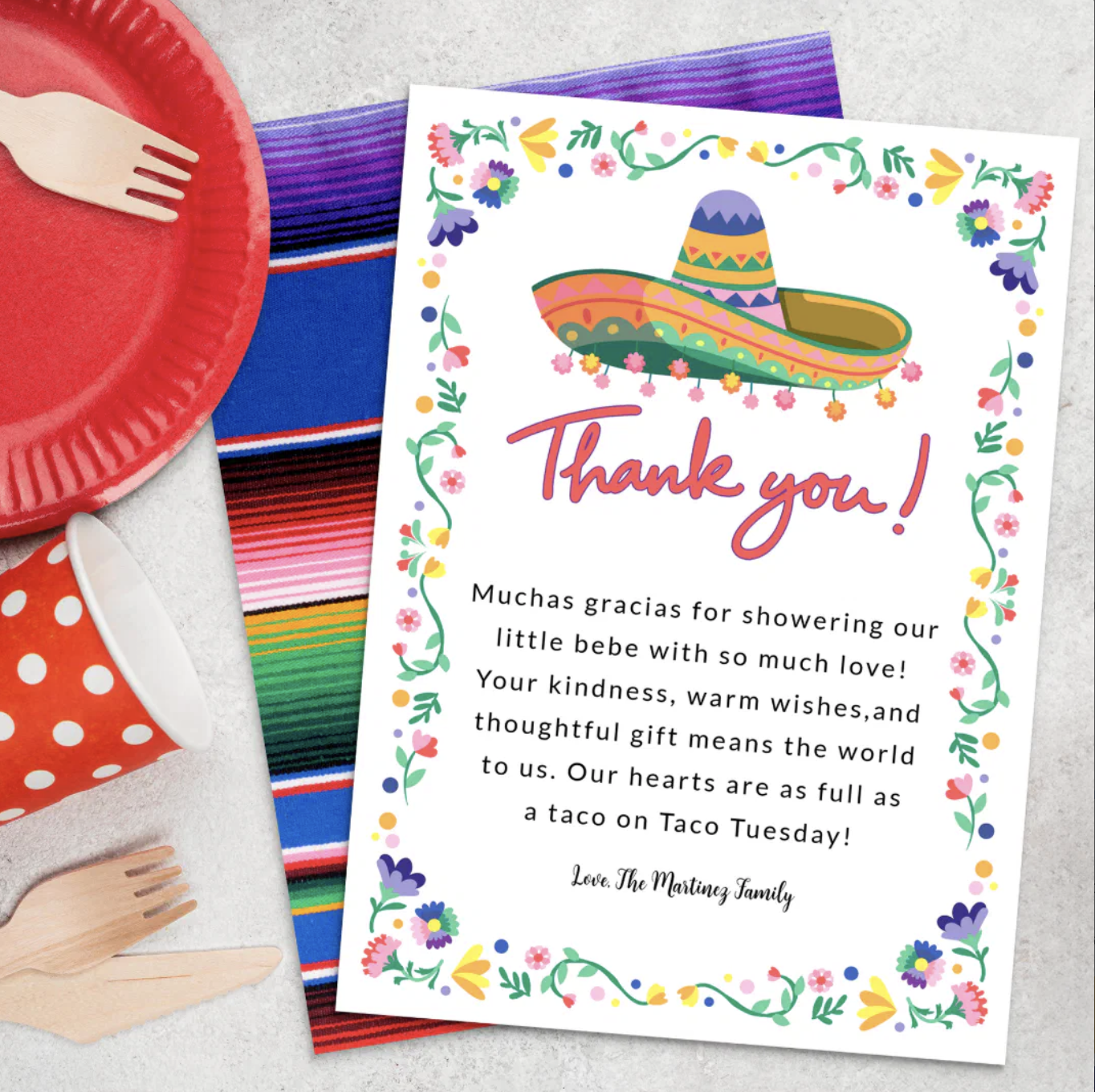 Fiesta baby shower thank you card with colorful floral border, sombrero illustration, and bright serape backdrop styled with red plates, cups, and festive tableware.