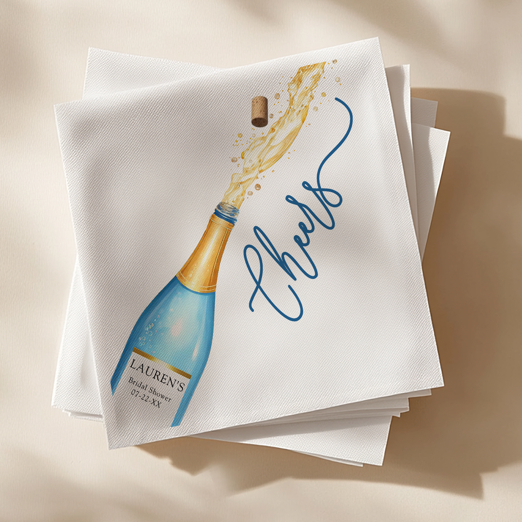 Square cocktail napkins with watercolor champagne bottle design and the word “Cheers” in elegant blue script.
