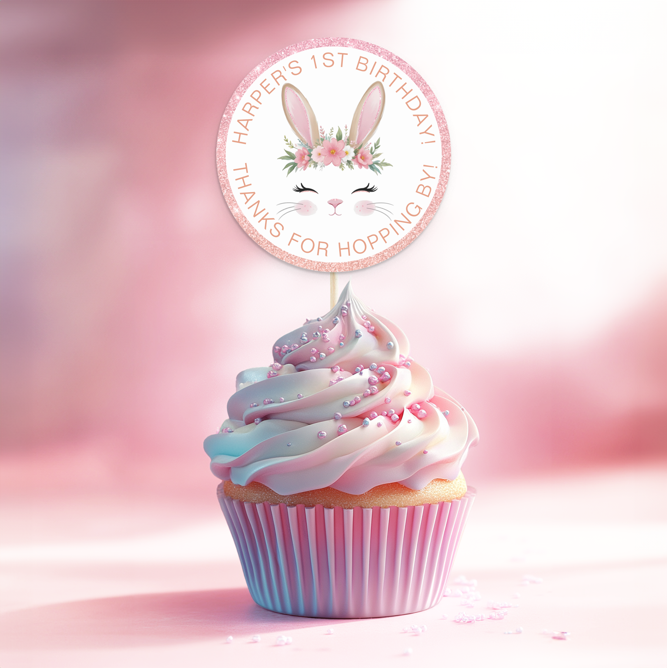 Some Bunny Is One round favor sticker with bunny face and pink glitter border, displayed as a cupcake topper.