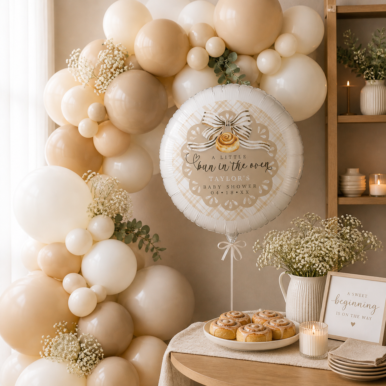Neutral baby shower balloon garland in cream, beige, ivory, tan, and white with Bun in the Oven themed balloon, cinnamon rolls, candlelight, and soft modern party décor.