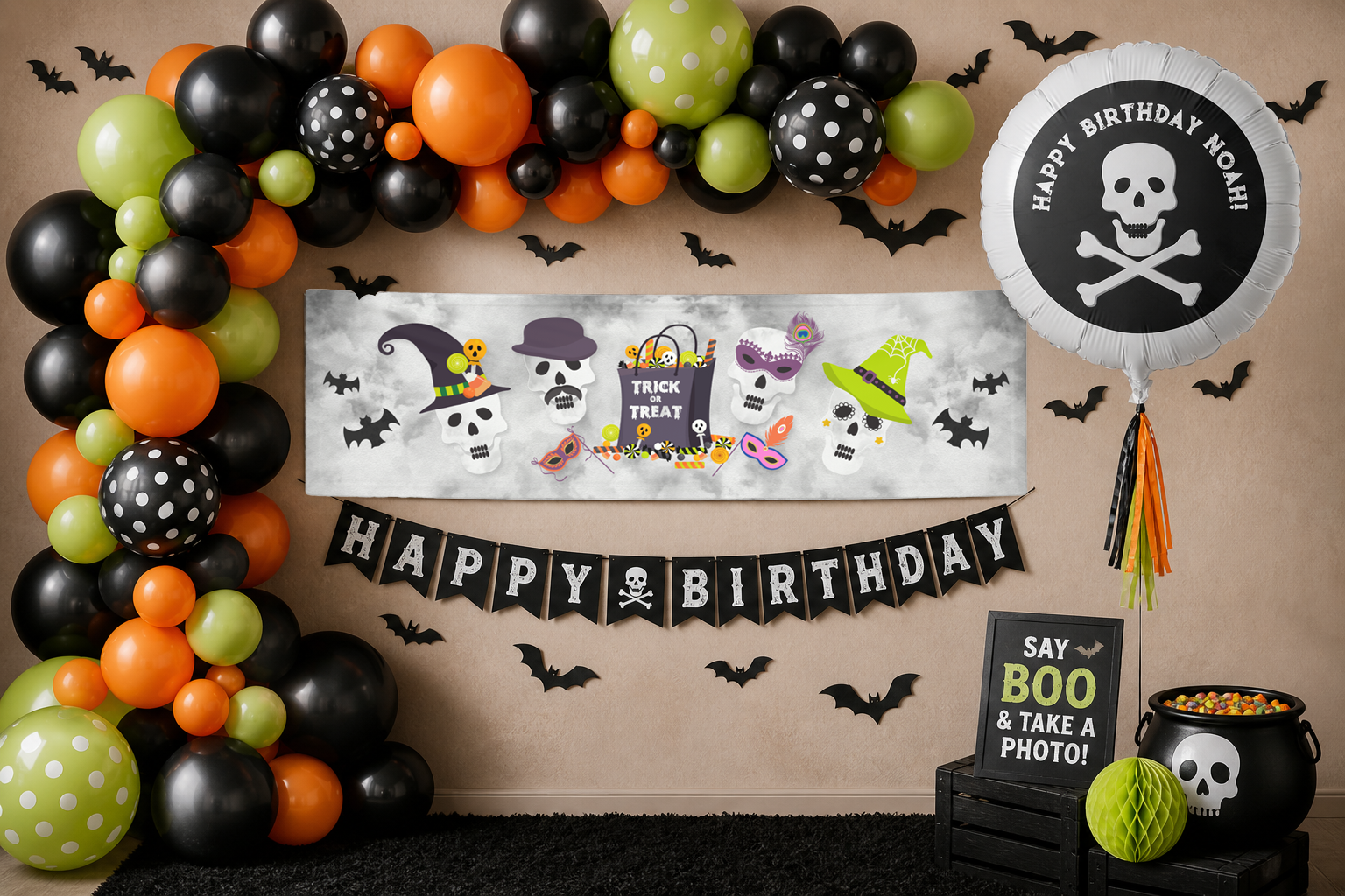 Halloween birthday photo backdrop featuring a black, orange, and green balloon garland, bat wall decorations, a themed banner, and a skull birthday balloon arranged for a festive party setup.