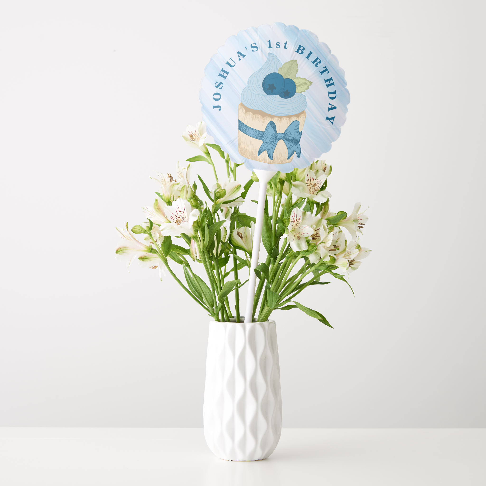 Blueberry cupcake first birthday balloon pick decoration displayed in a white vase with flowers.
