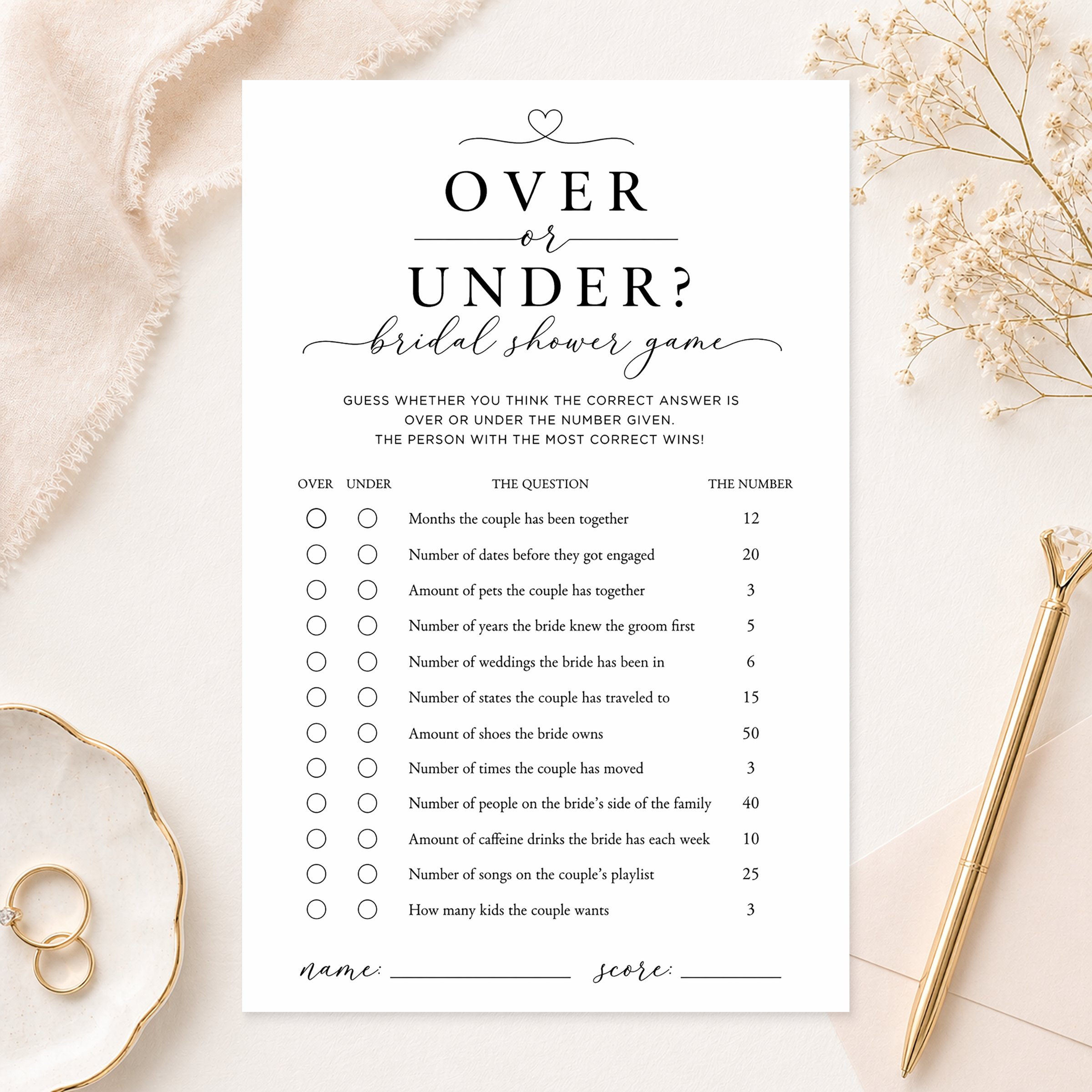 Elegant Over or Under bridal shower game card displayed in a neutral flat lay with gold pen, ring dish, soft fabric, and floral accents. Minimalist black and white bridal shower trivia game with over or under guessing questions.