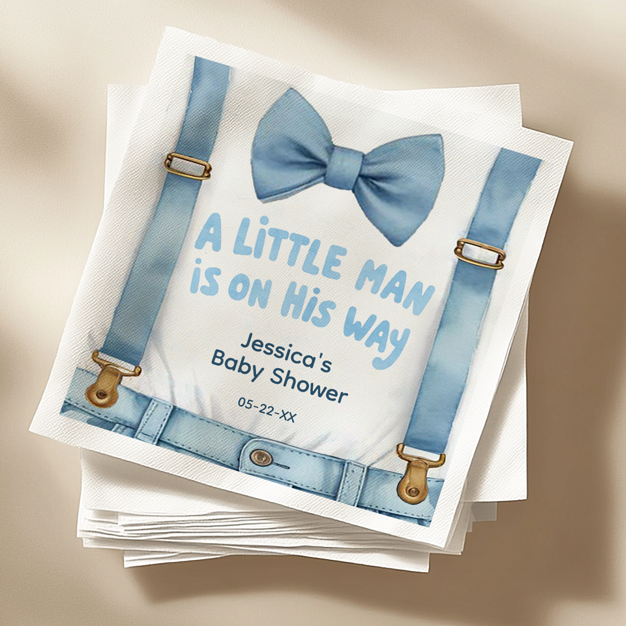 Stack of personalized baby shower napkins featuring a watercolor blue bow tie and “A Little Man Is On His Way” design.