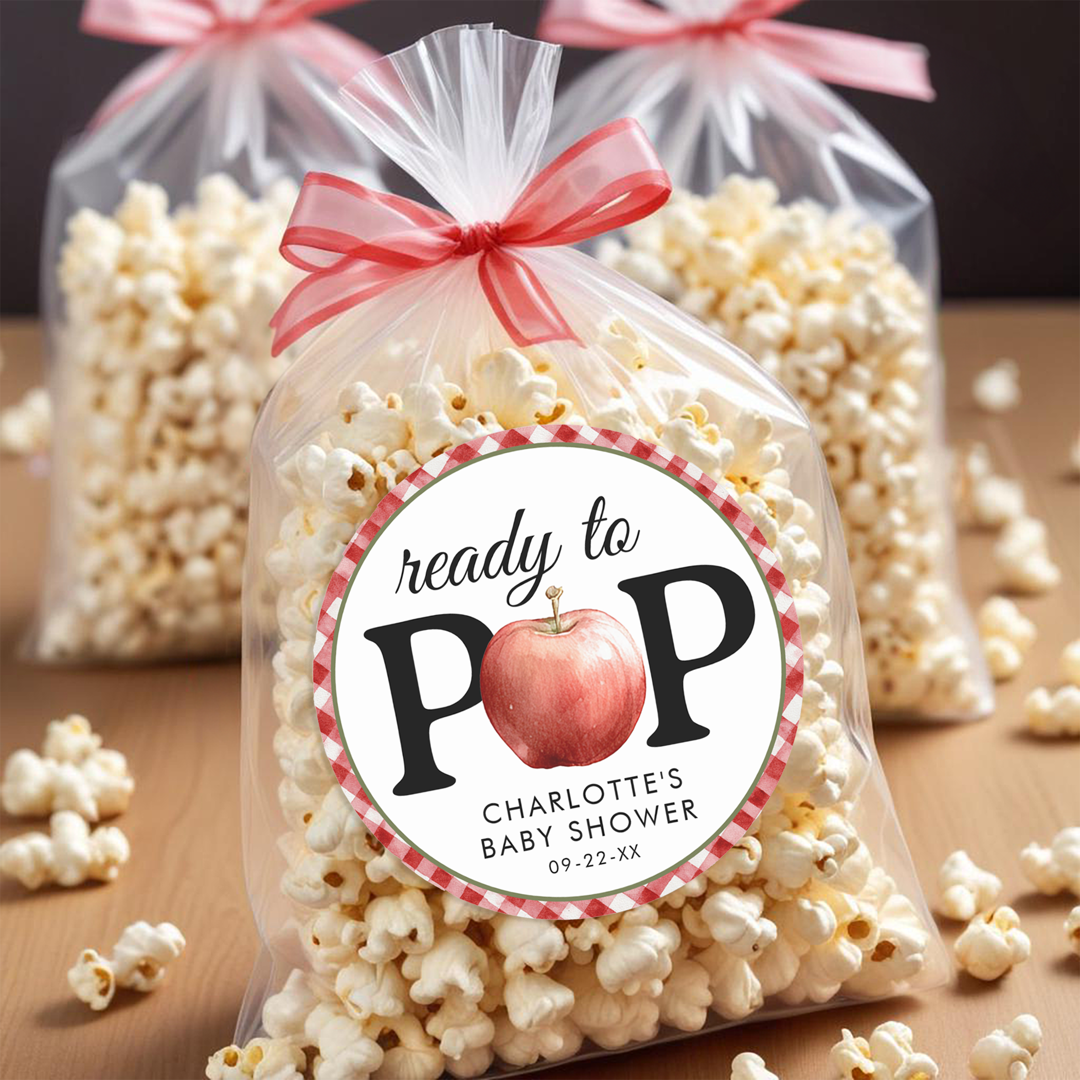Apple of Our Eye baby shower popcorn favor bags with personalized Ready to Pop stickers featuring apple design and red gingham border.