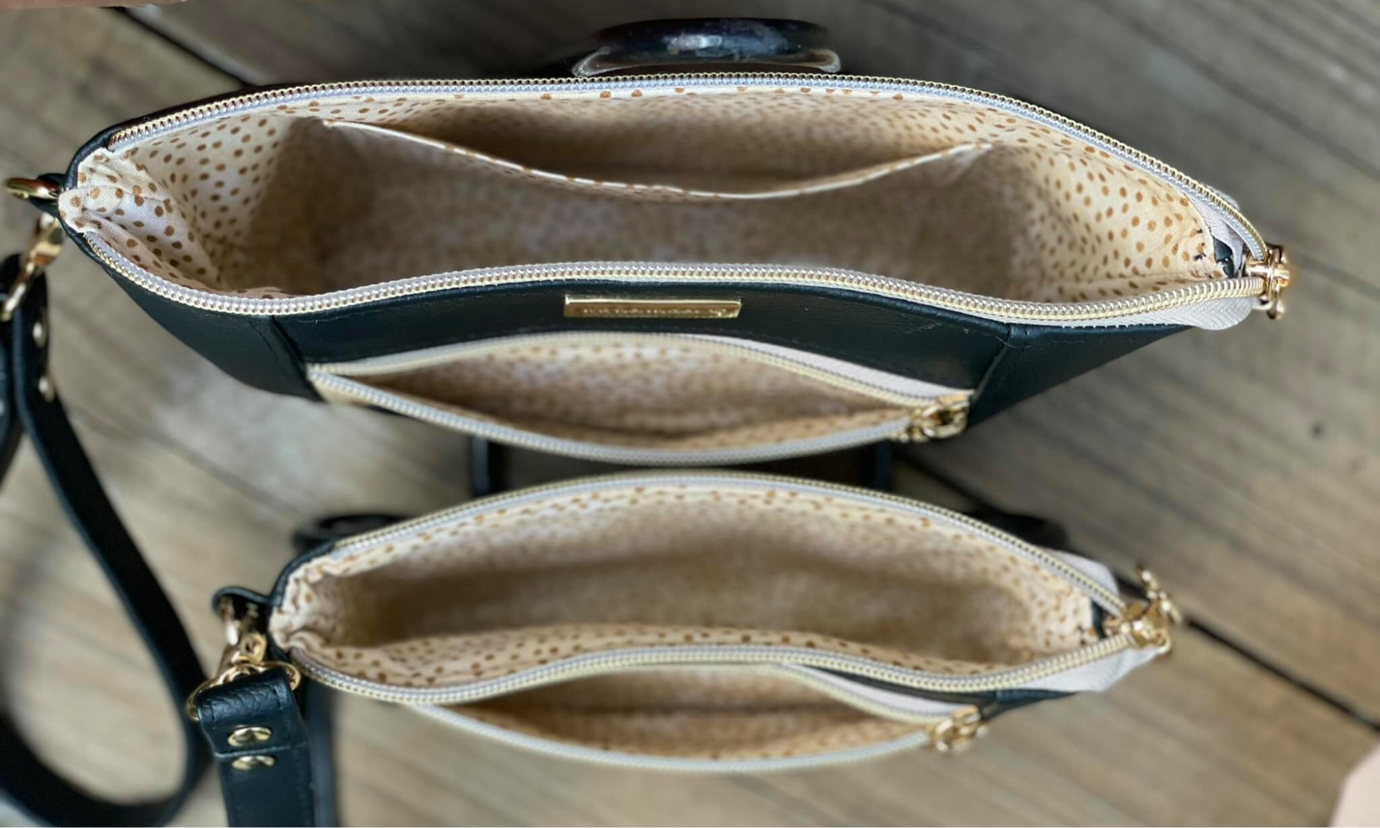 Two black handbags with gold zippers and beige polka dot fabric interior, photographed from above on a wooden surface.