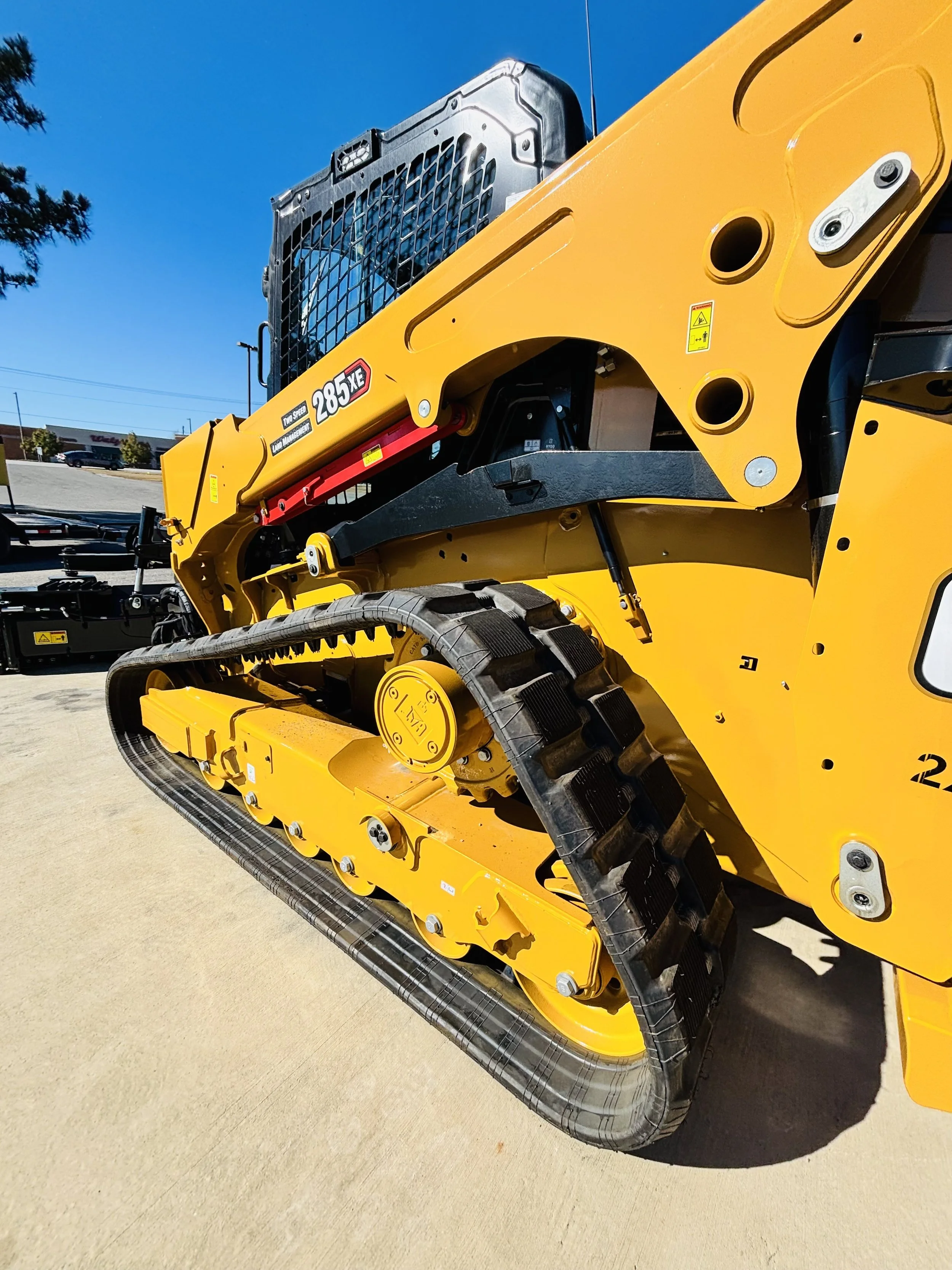 Close-up of a yellow compact track loader, model 285 XE, parked on a concrete surface under a clear blue sky.