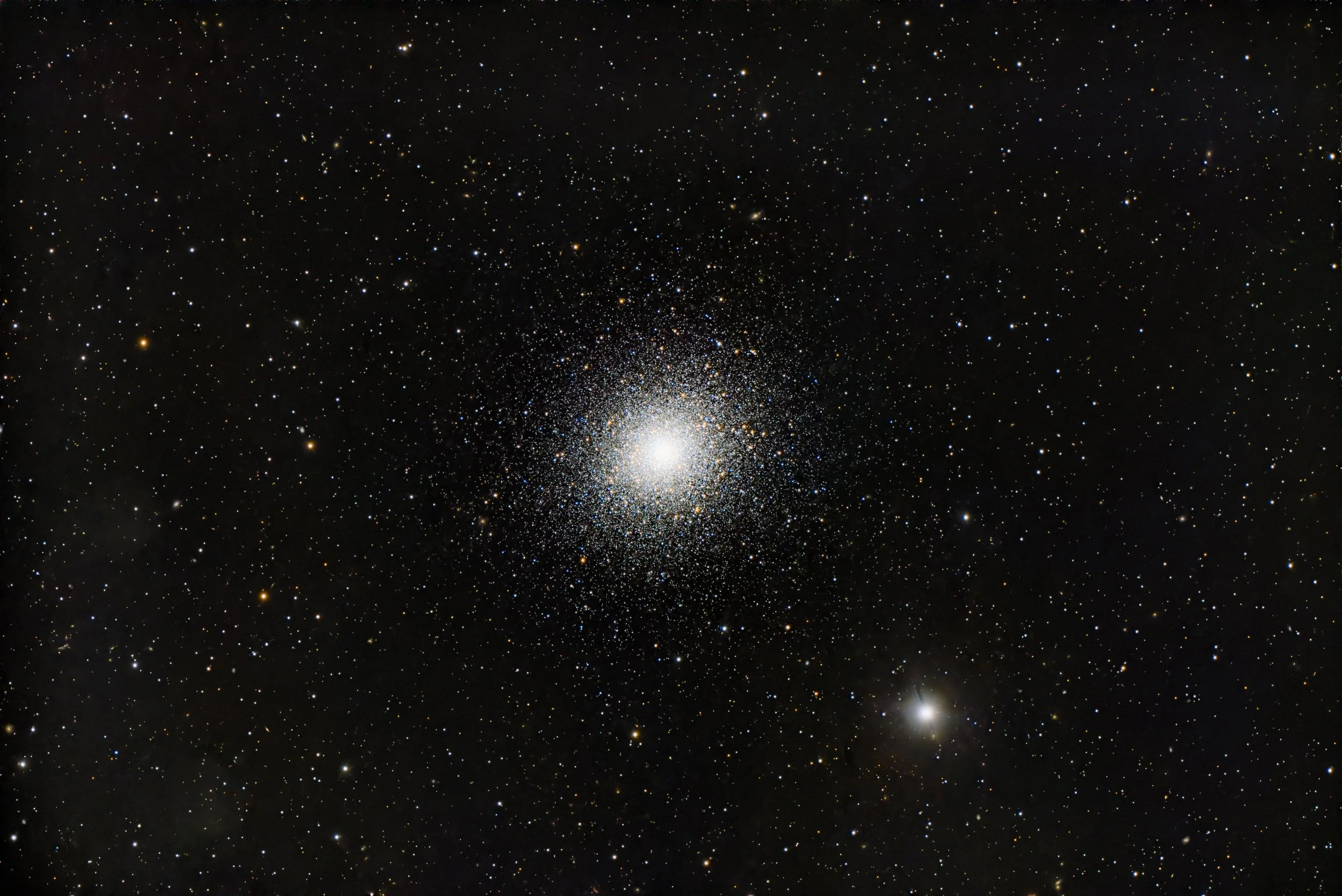 A view of deep space with numerous stars and a bright, densely packed cluster of stars at the center.