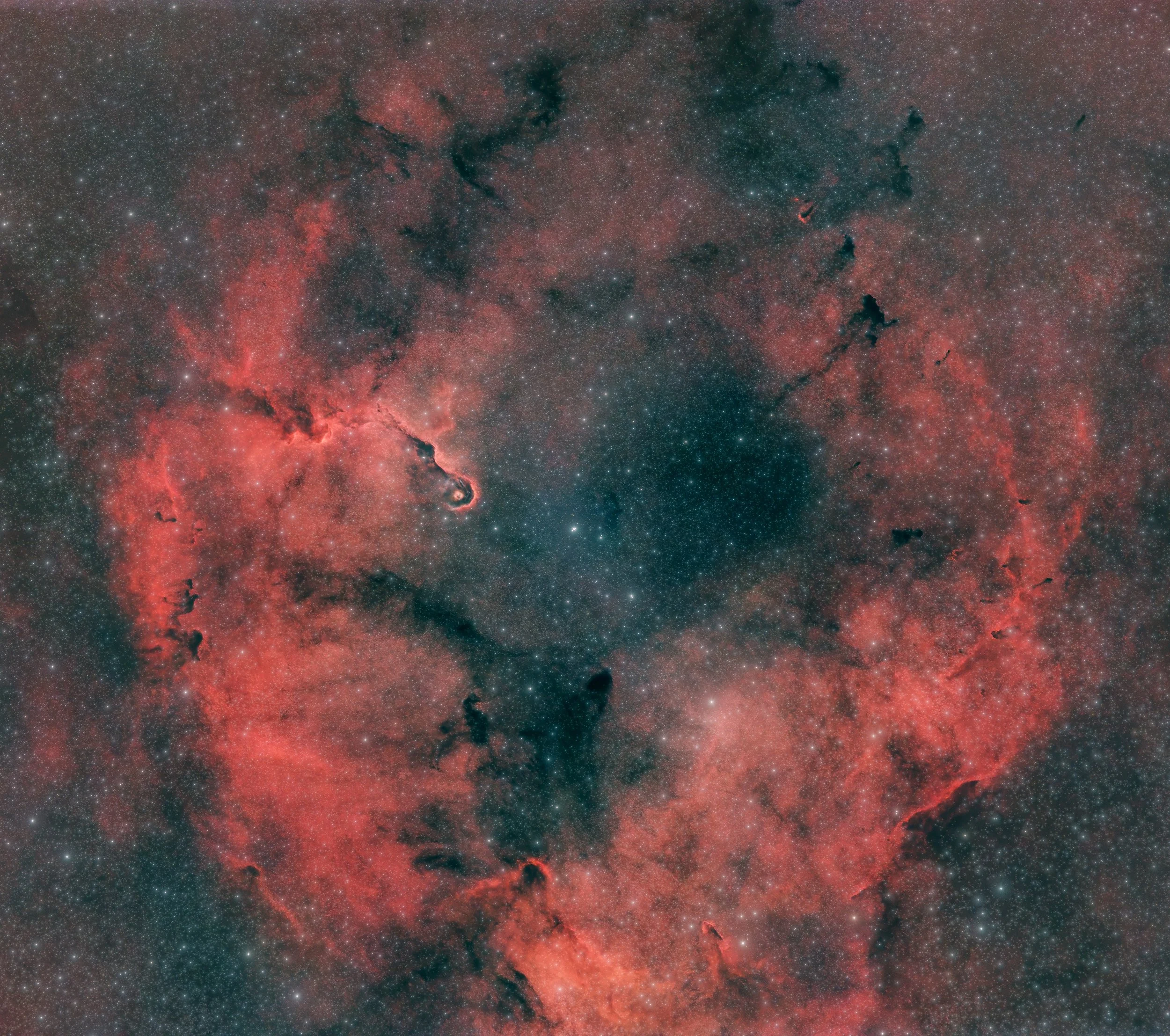 A detailed image of a nebula in deep space with numerous stars, dark cloudy regions, and reddish illuminated areas, showcasing the beauty of a cosmic star-forming region.