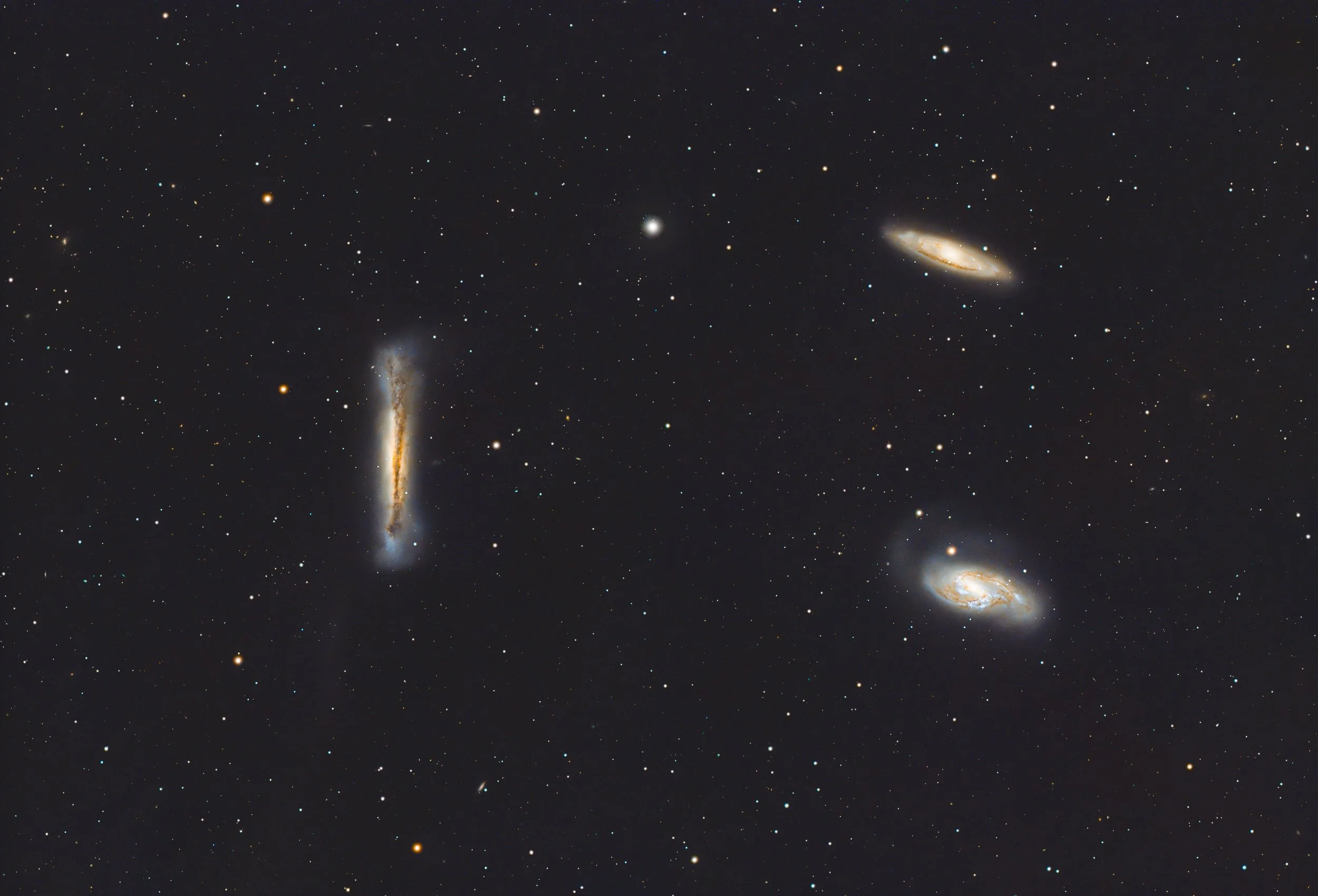 A wide view of outer space showing numerous stars and several distant galaxies, including a spiral galaxy at the bottom right, an elongated galaxy near the middle, and a fuzzy galaxy cluster at the bottom left.