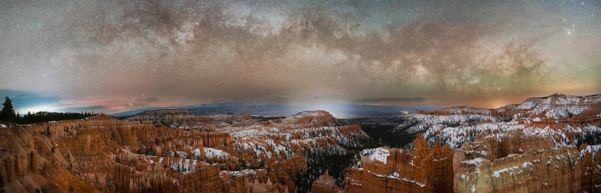 Night sky with the Milky Way galaxy visible over a snow-capped canyon landscape.
