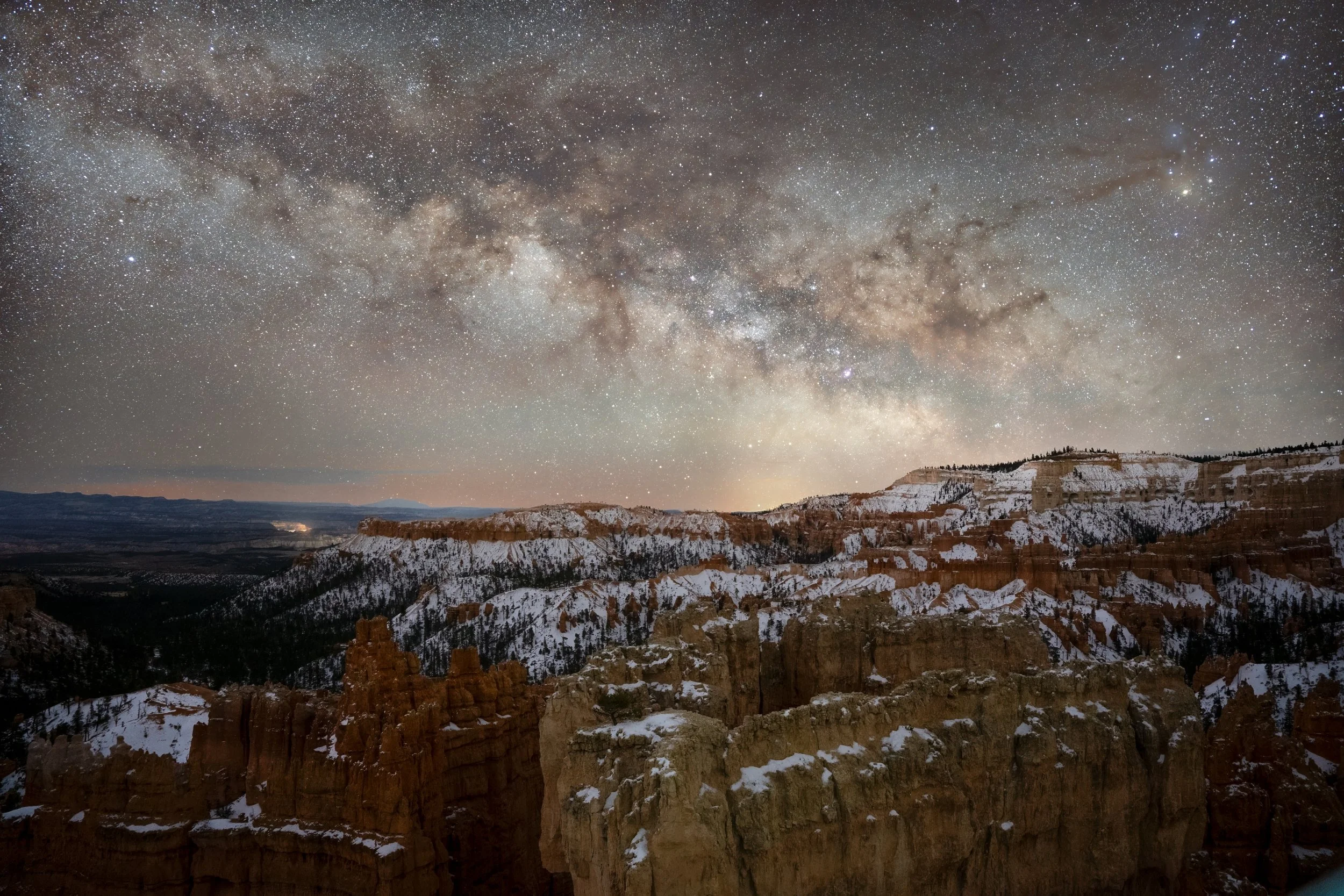 Night sky filled with stars and the Milky Way galaxy over Snowy canyon with cliffs and rock formations