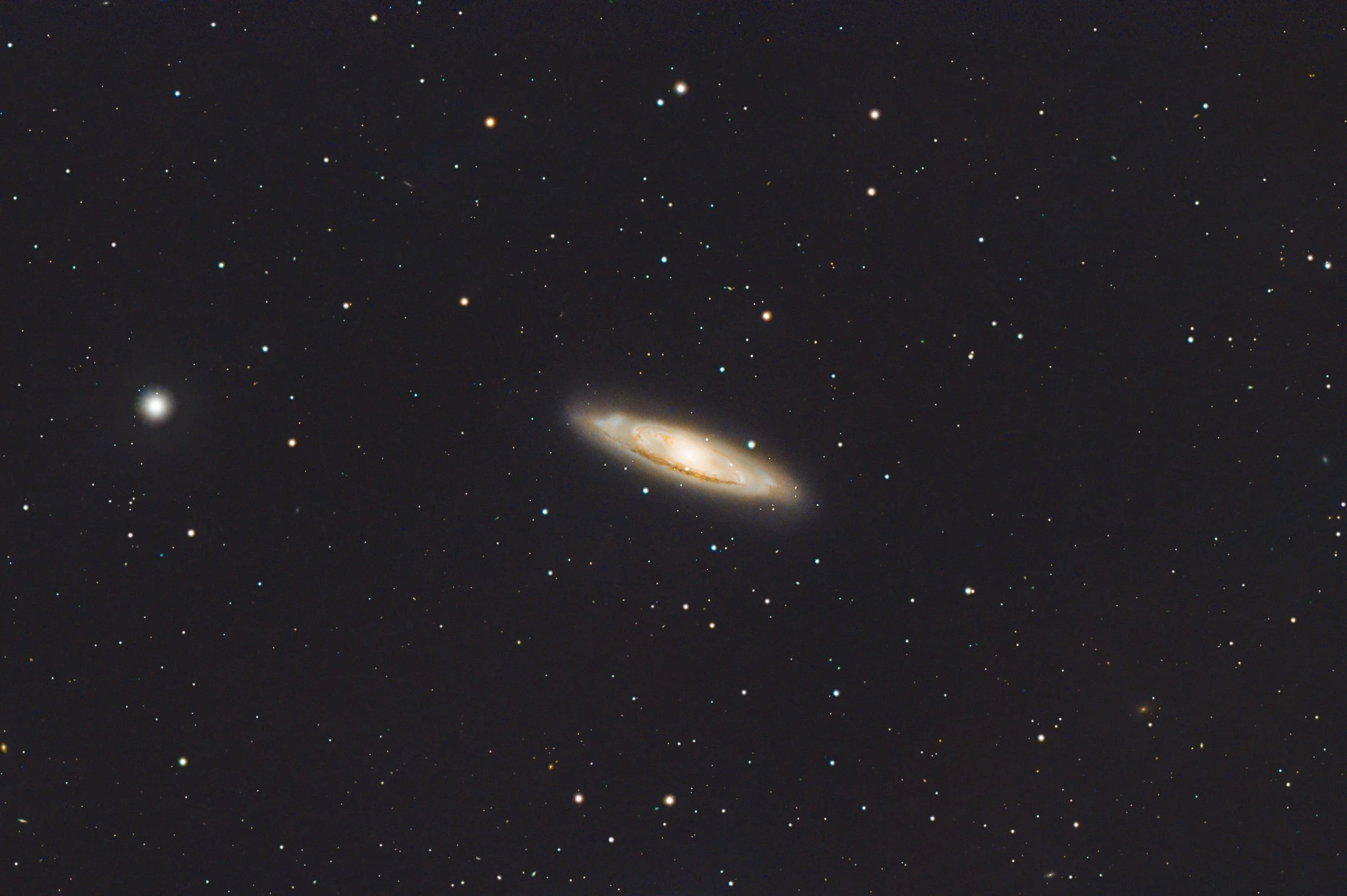 A view of space featuring numerous stars, a spiral galaxy near the bottom, and some distant celestial objects scattered across the dark sky.