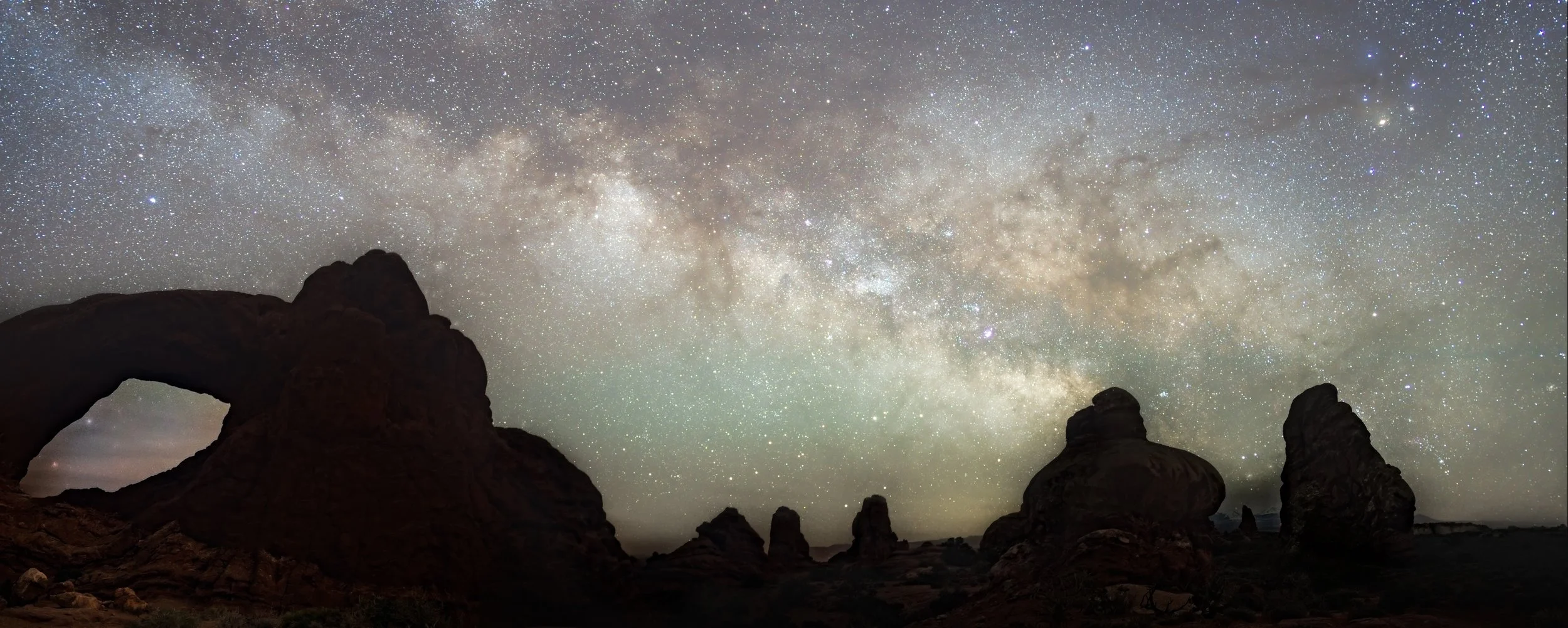 Night sky filled with stars and the Milky Way galaxy over desert rock formations at night.