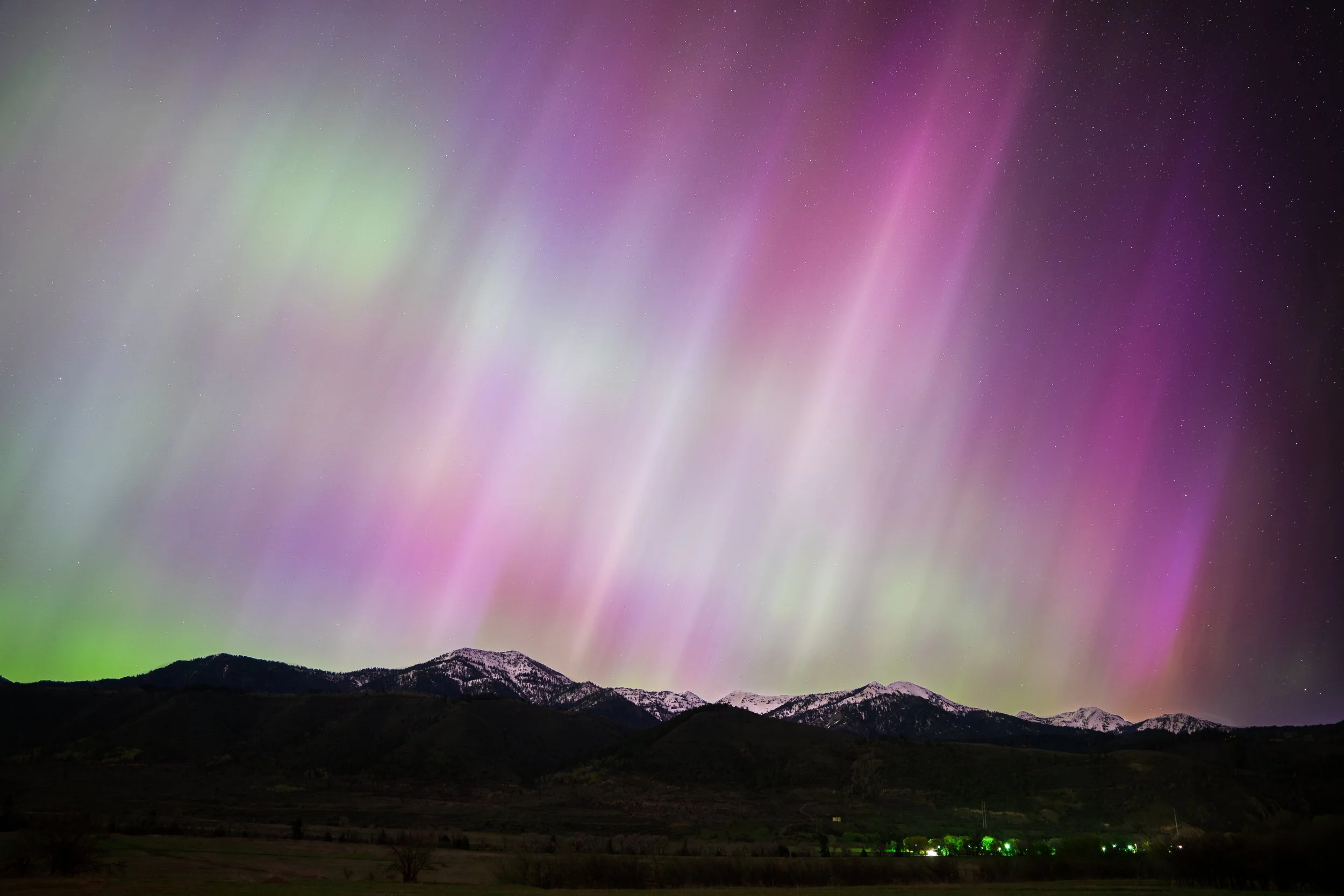 Northern Lights over snow-capped mountains at night, with a starry sky and a dark landscape in the foreground.