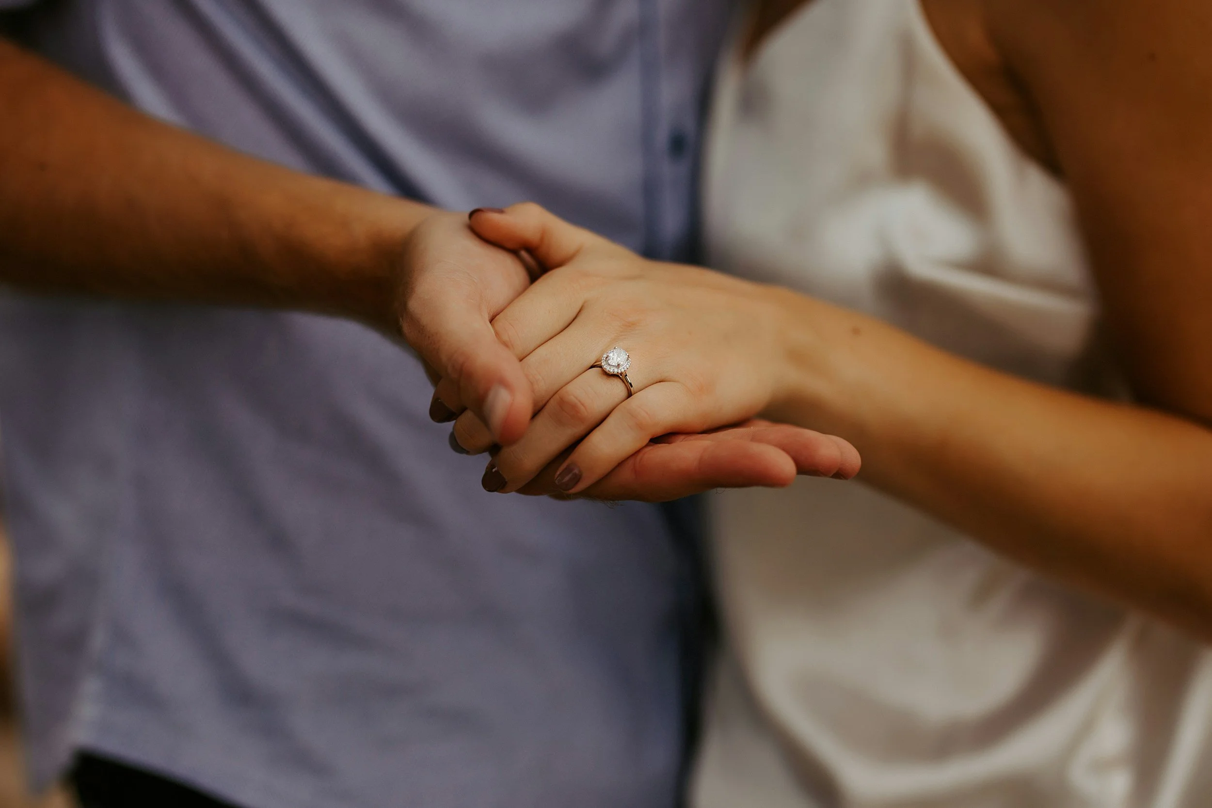 A close-up of two people holding hands, with one person wearing a diamond ring on their ring finger.
