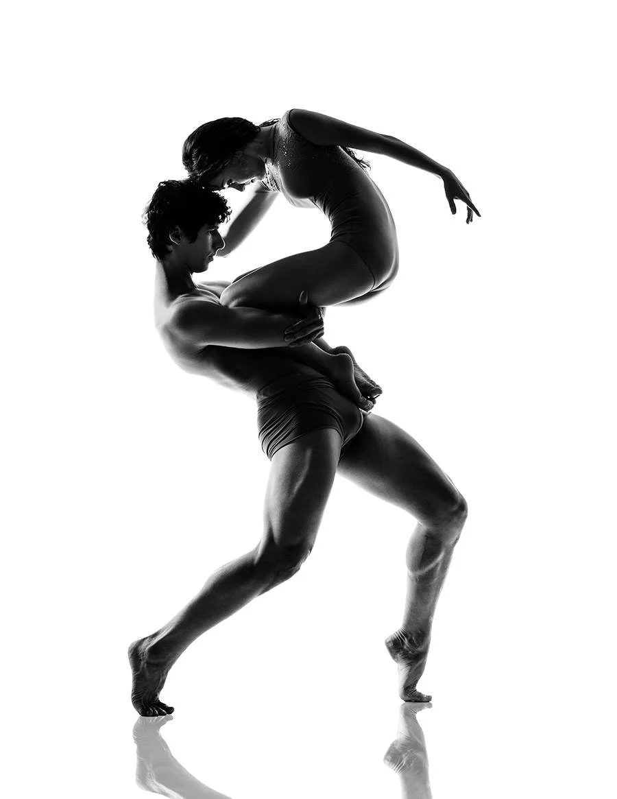 Silhouetted dance partners, a man and a woman, in a contemporary dance pose, with the man lifting the woman in a high, curved arch.