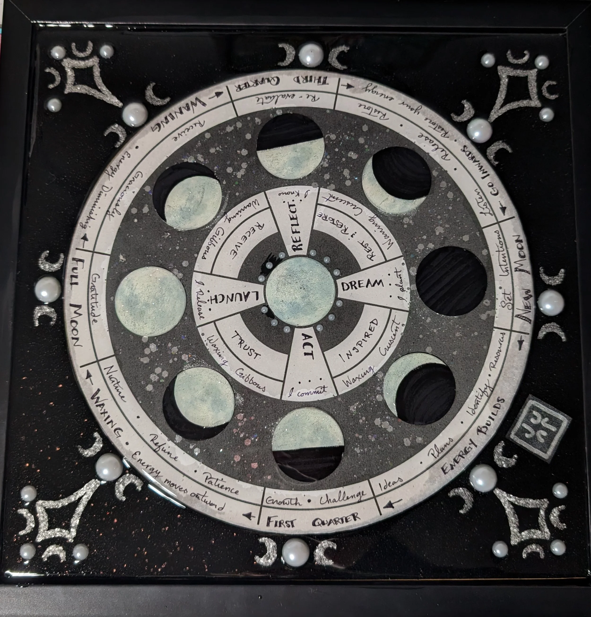 Decorative circular board with moon phases, motivational words, and a cosmic theme featuring black, white, and silver accents.
