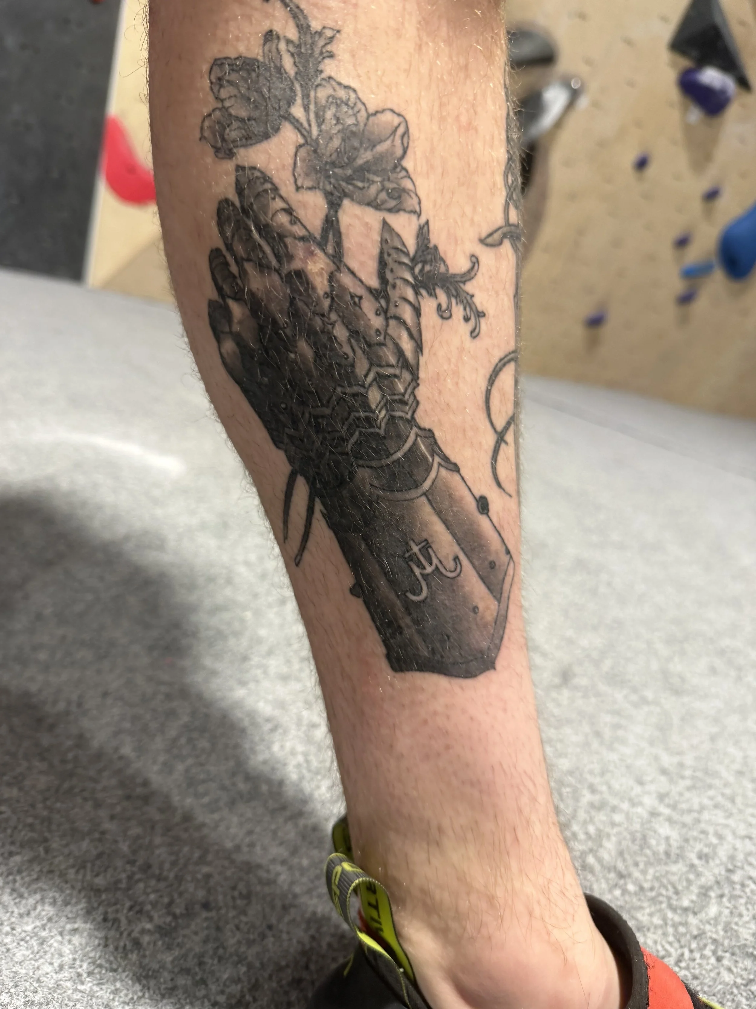 Black tattoo of a potted plant or flower with leaves on a person's lower leg.