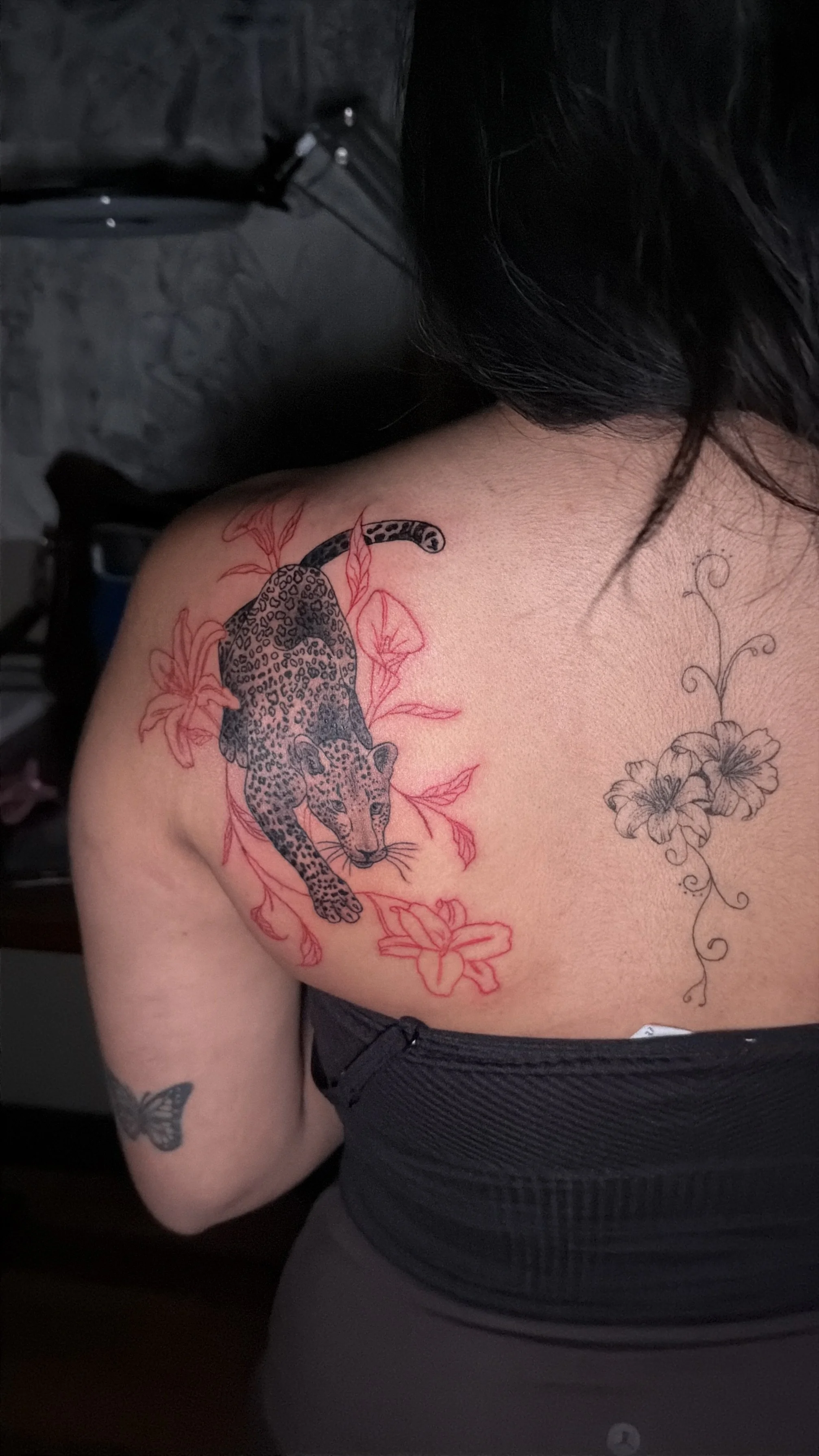 Tattoo of a leopardess with leopard spots and surrounded by pink and black floral designs on woman's shoulder and upper arm.