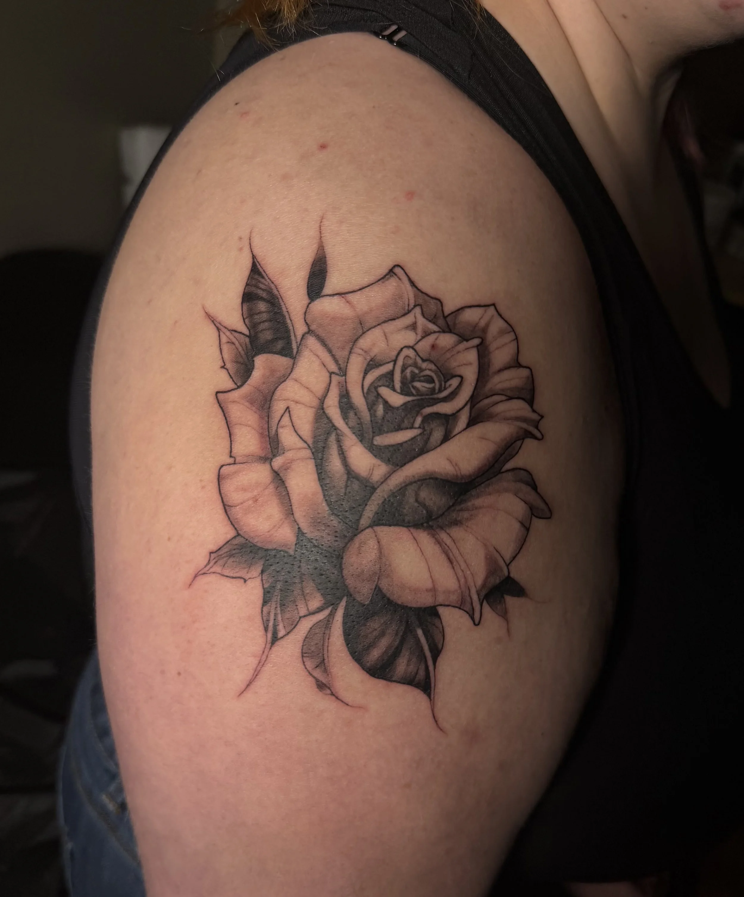Black and gray rose tattoo on person's upper arm.