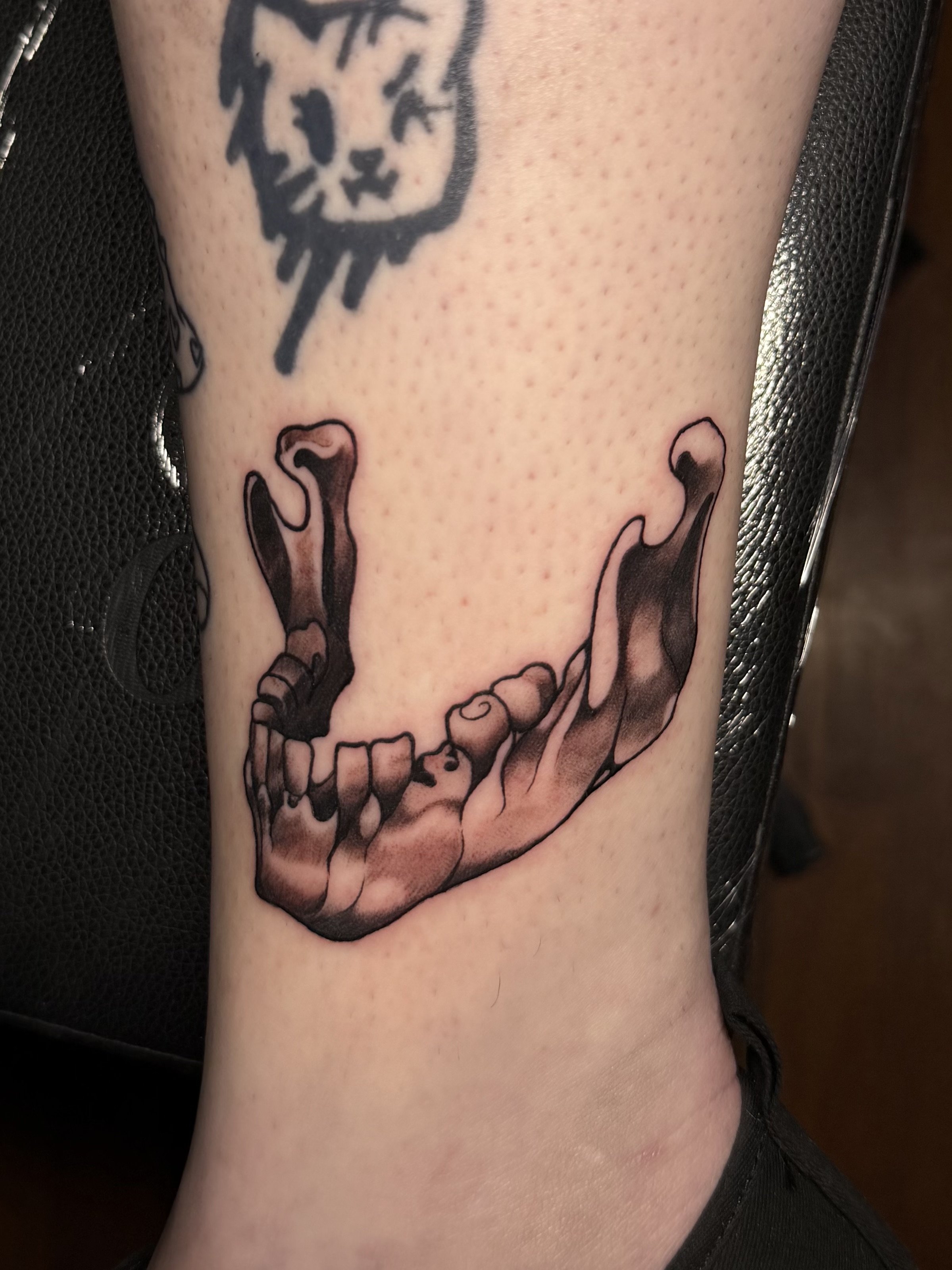Tattoo of a detailed human jawbone with teeth on a person's leg.