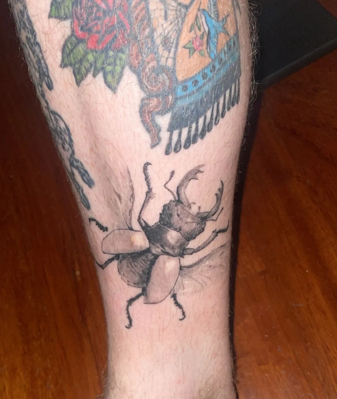 Tattoo of a bee on a person's leg with other tattoos partially visible nearby.