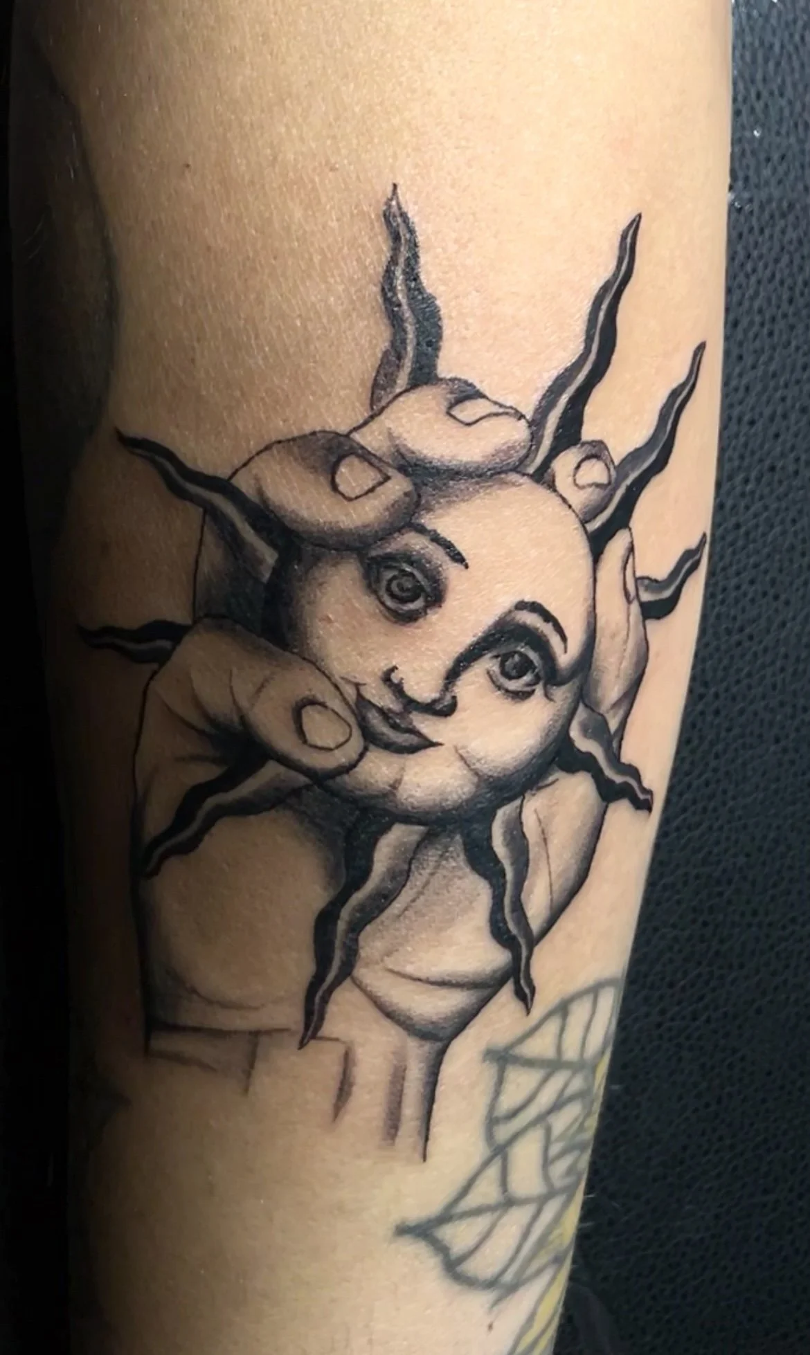 Tattoo of a happy sun with human facial features and a hand resting on its chin.