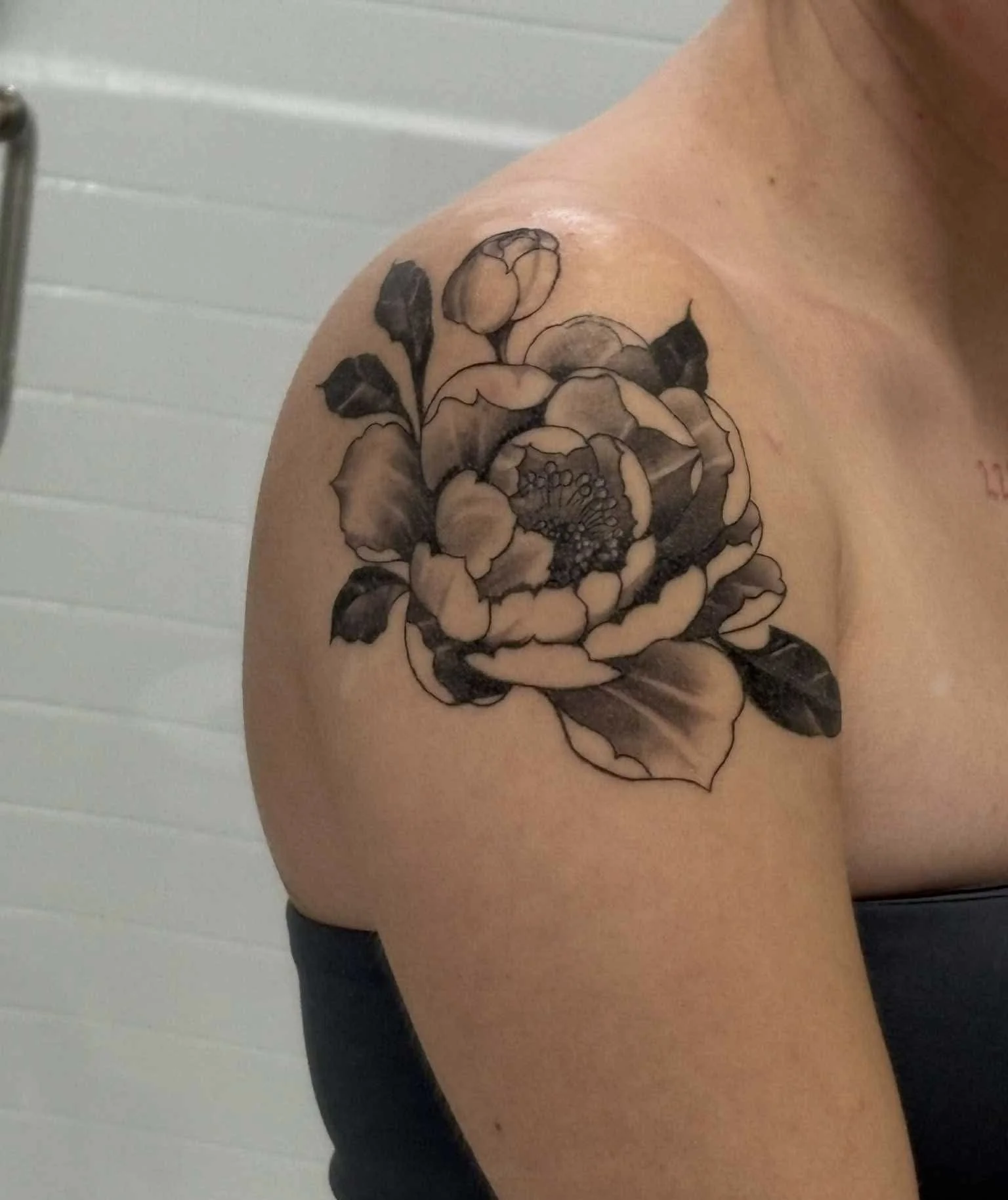 Black and gray ink floral tattoo on person's upper arm featuring a large blooming flower.