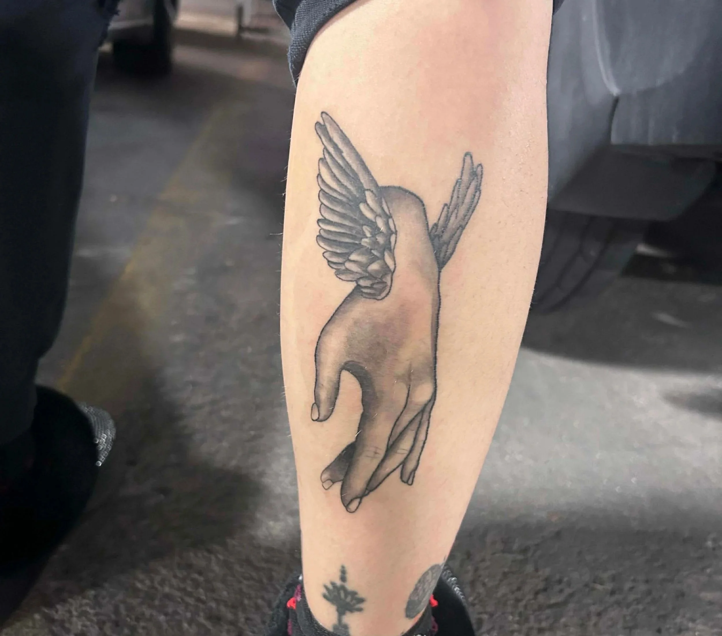 A tattoo of a hand with wings on the forearm.