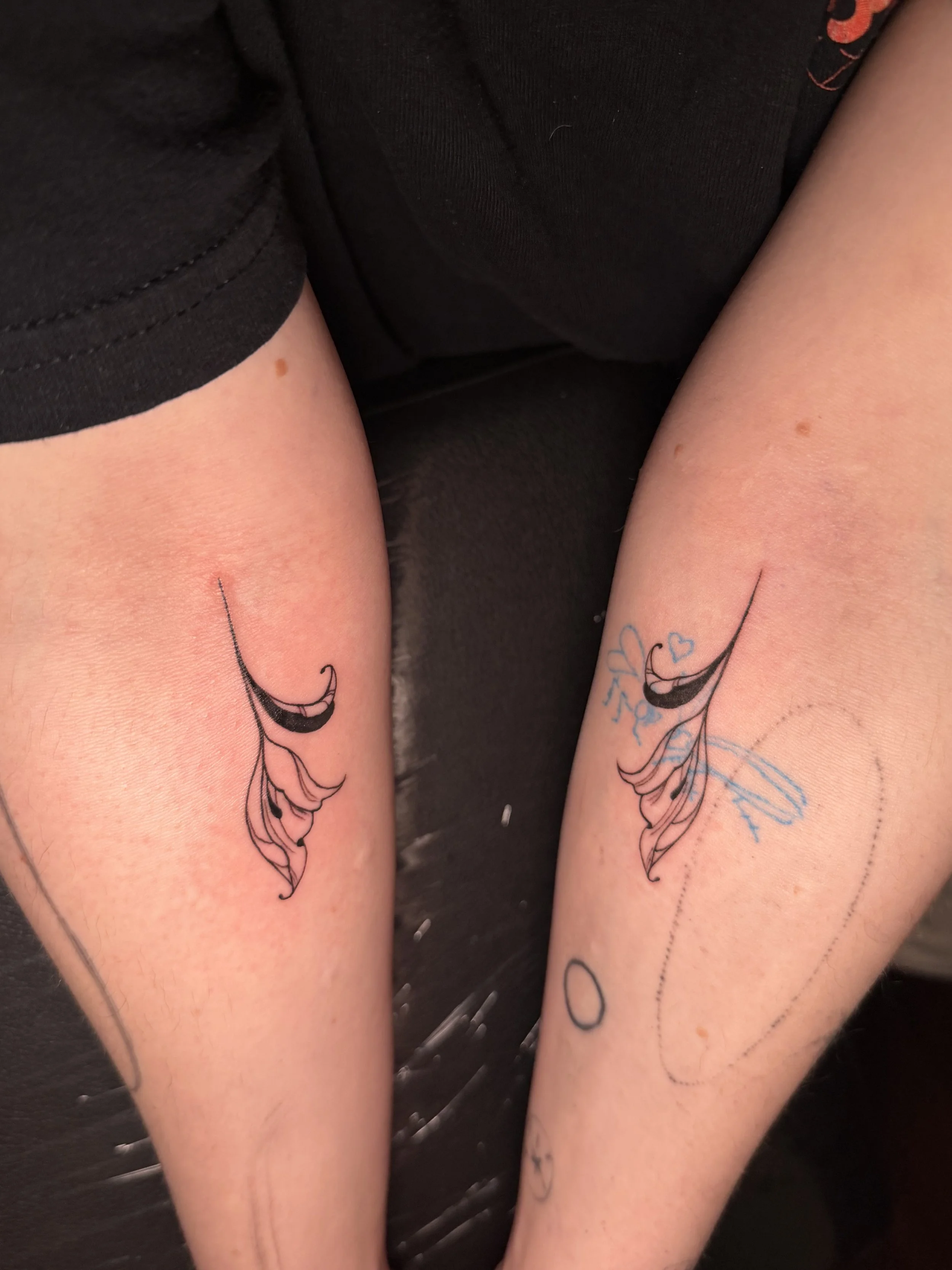 Two forearms with matching black and pink floral tattoos resting on a black surface.
