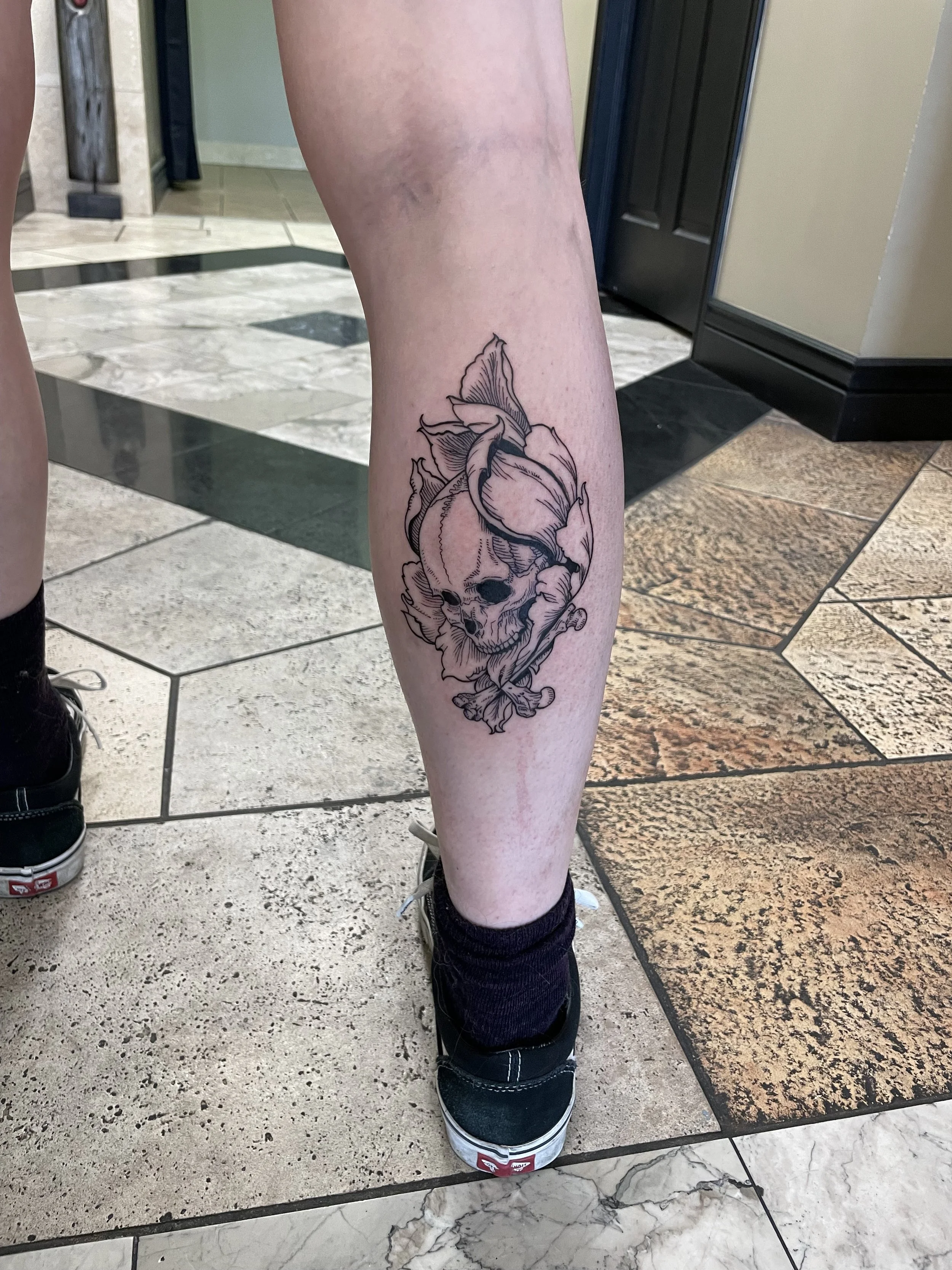 Tattoo of a skull entwined with a rose on a person's lower leg.