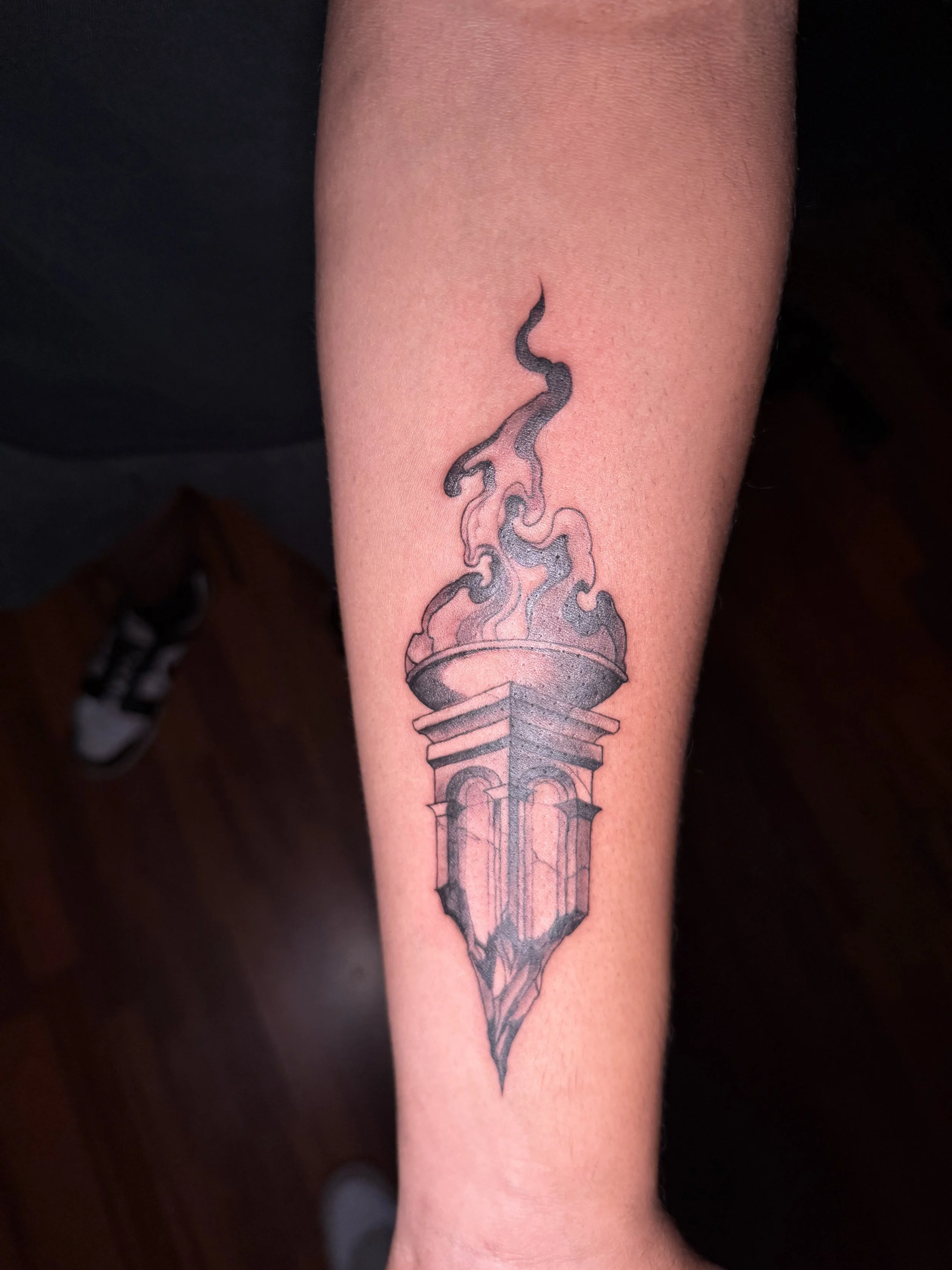 Tattoo of a flaming torch on a person's forearm.