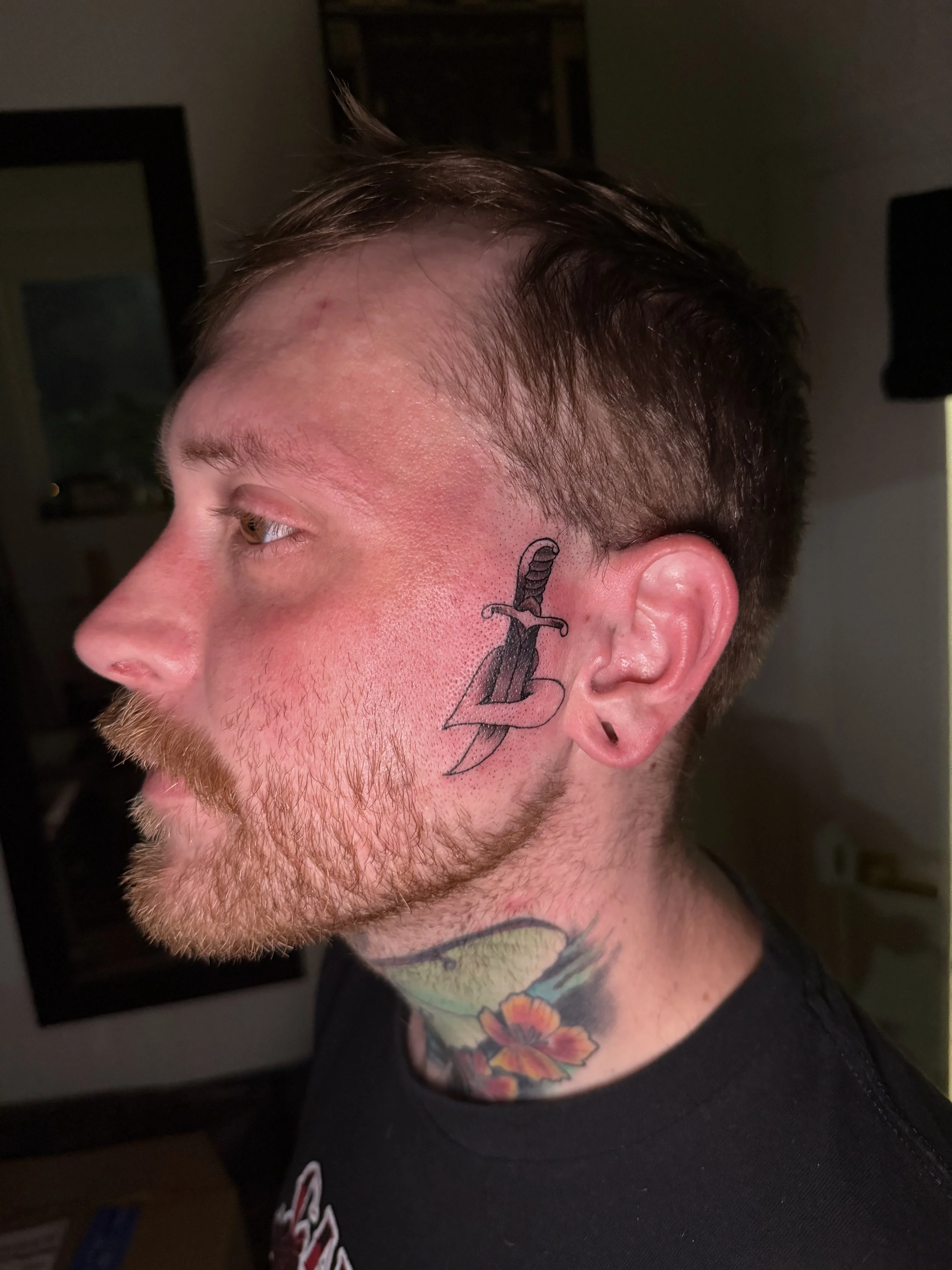 A man with tattoos on his neck and face, looking to the left, in an indoor setting.