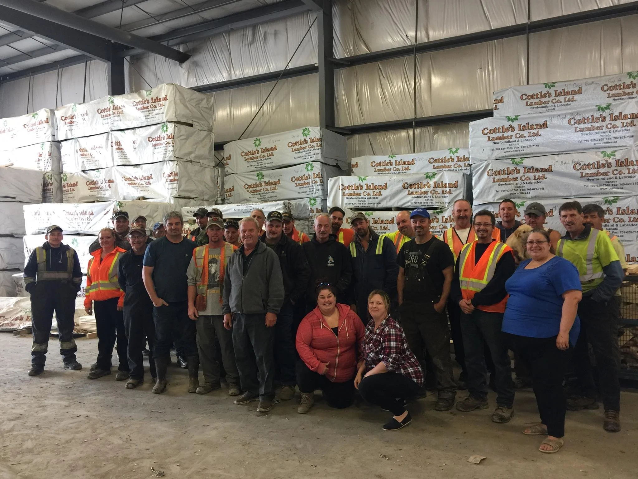 A group of people posing inside a warehouse with large bags of lumber in the background.