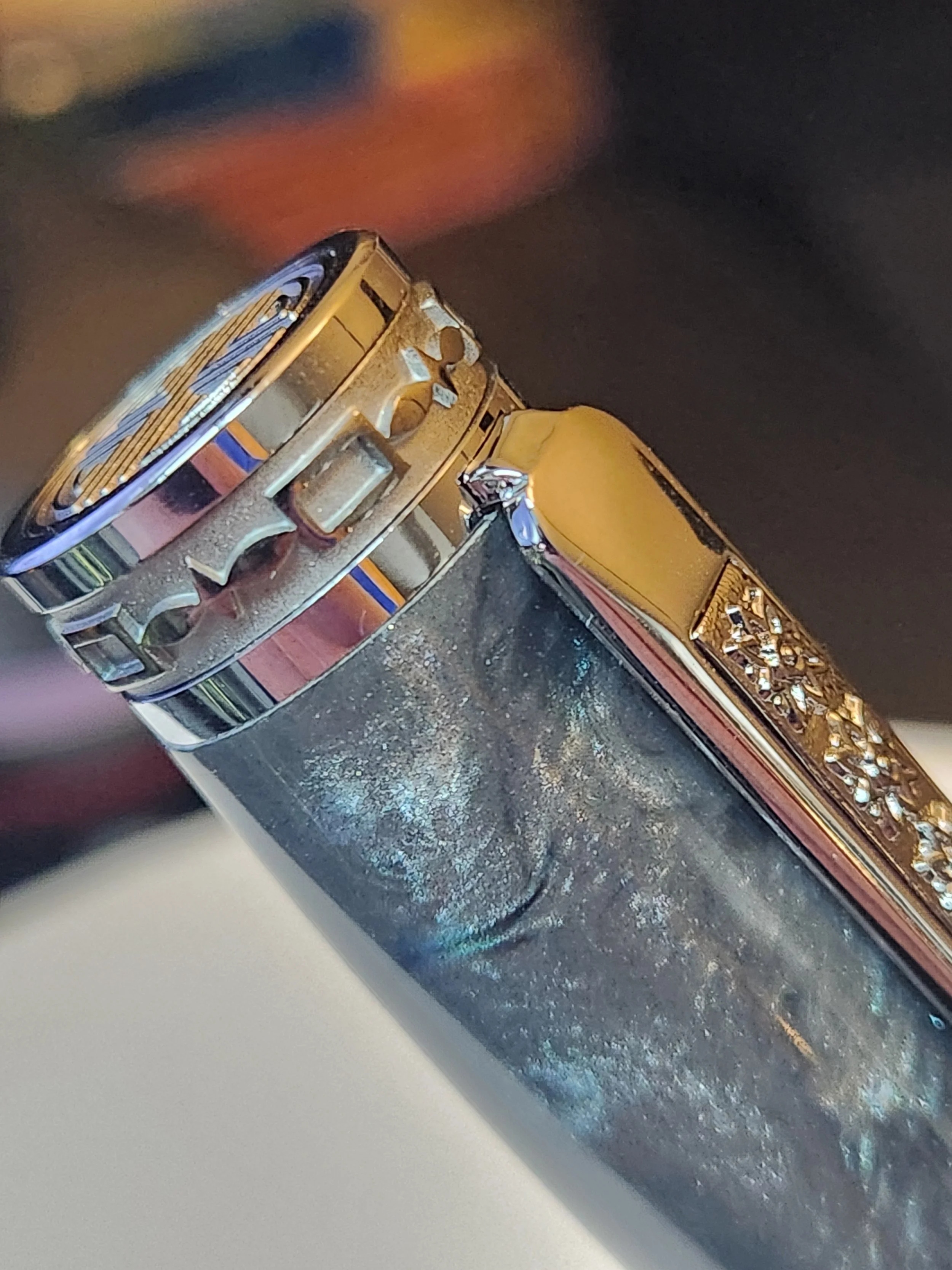 Close-up of a metallic lighter with a decorative top, showing the ignition wheel and design details, against a blurred dark background.